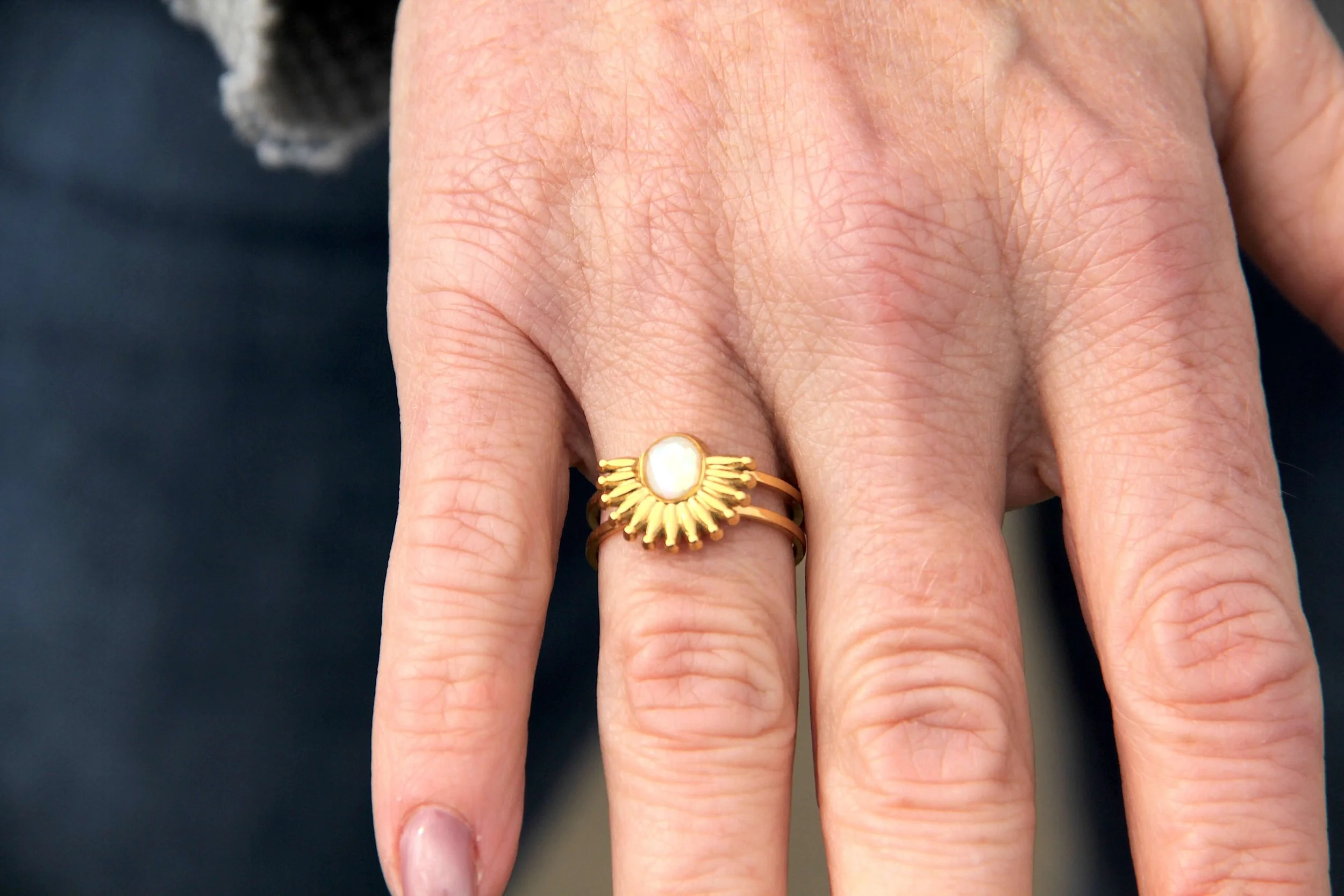 A close up of a woman wearing an abalone shell gold ring on her finger.