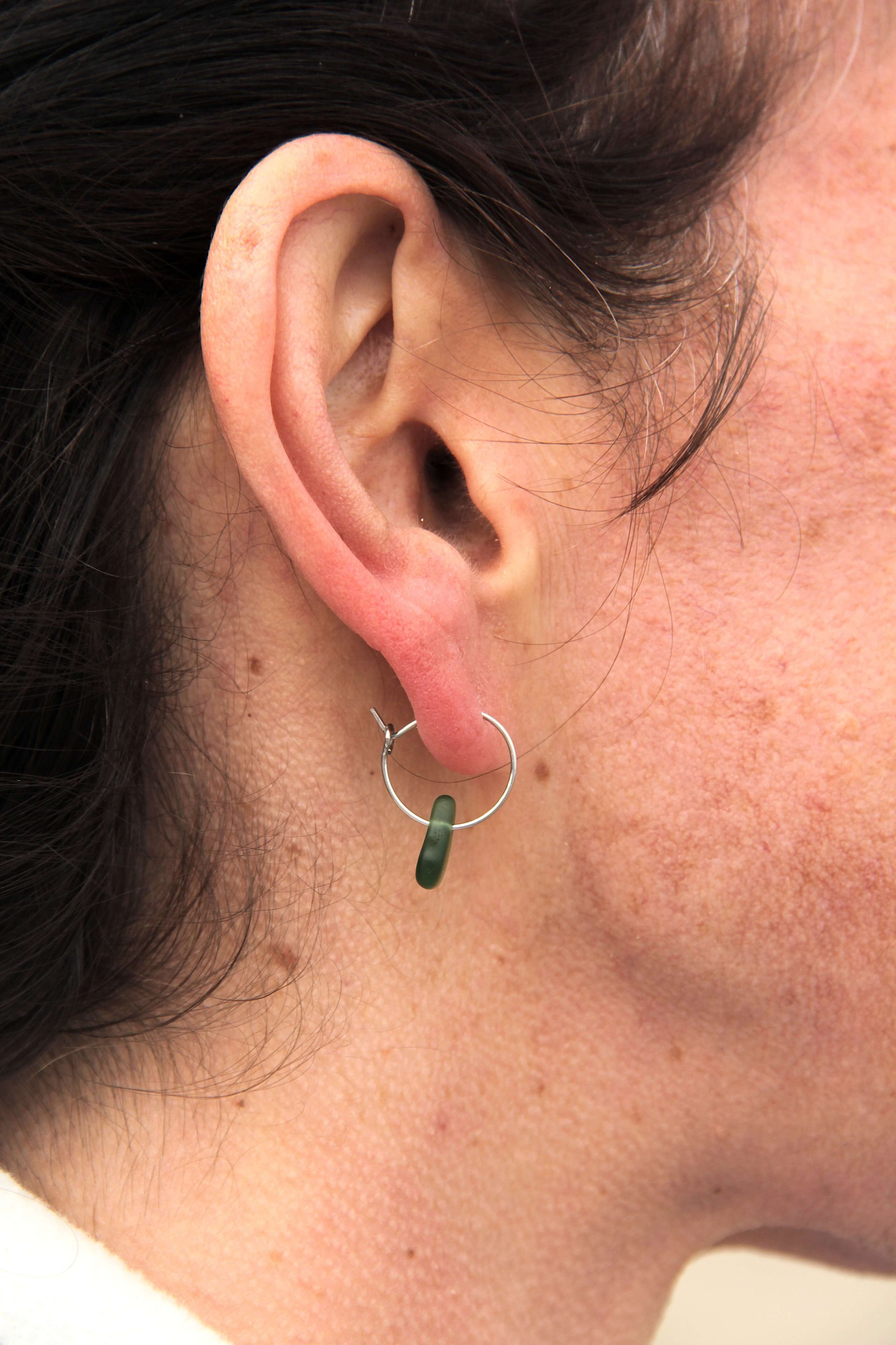 Close up of woman wearing a silver stainless steel sea glass hoop earring on her ear.