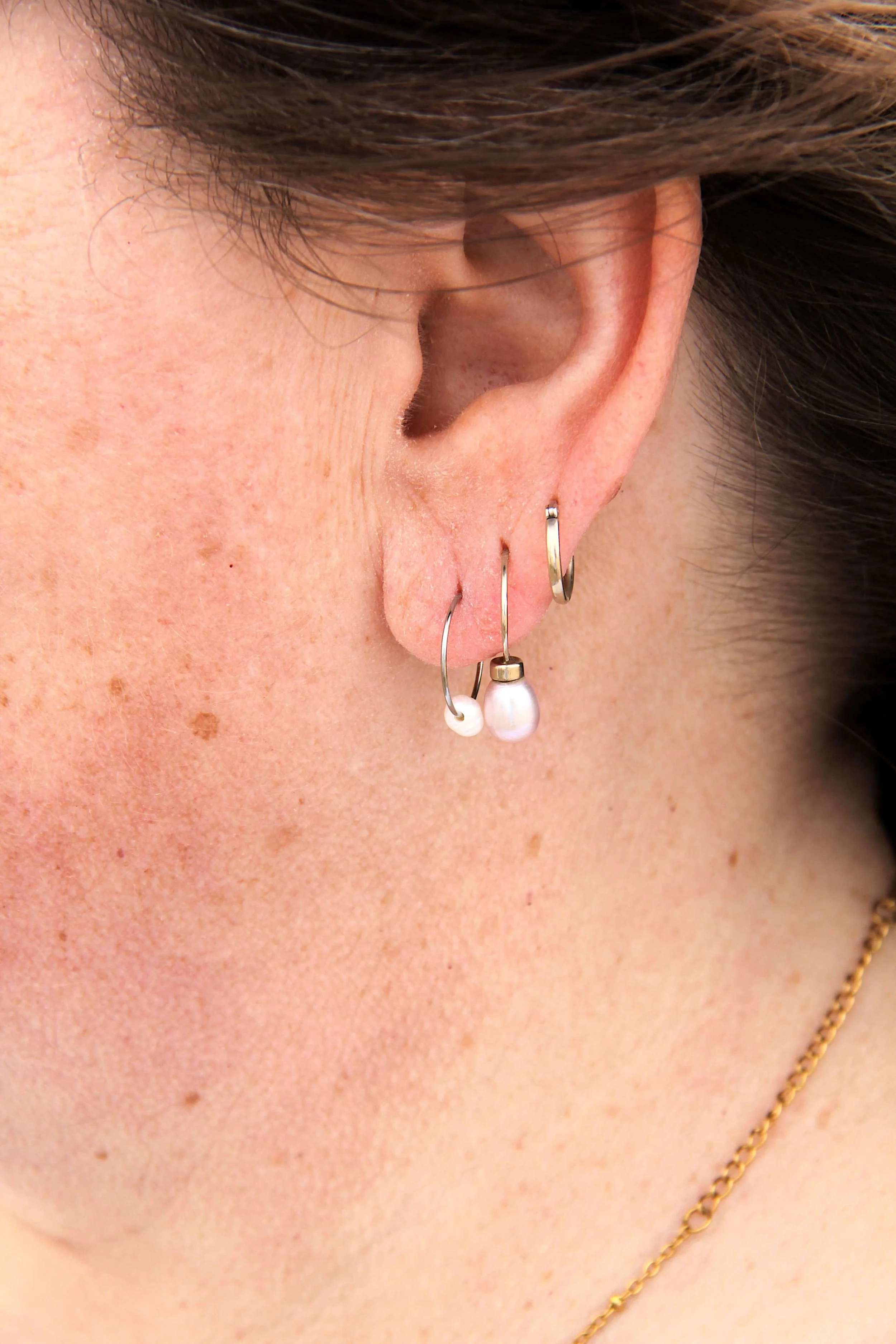 Close up of woman wearing a silver stainless steel freshwater pearl hoop earring on her ear.