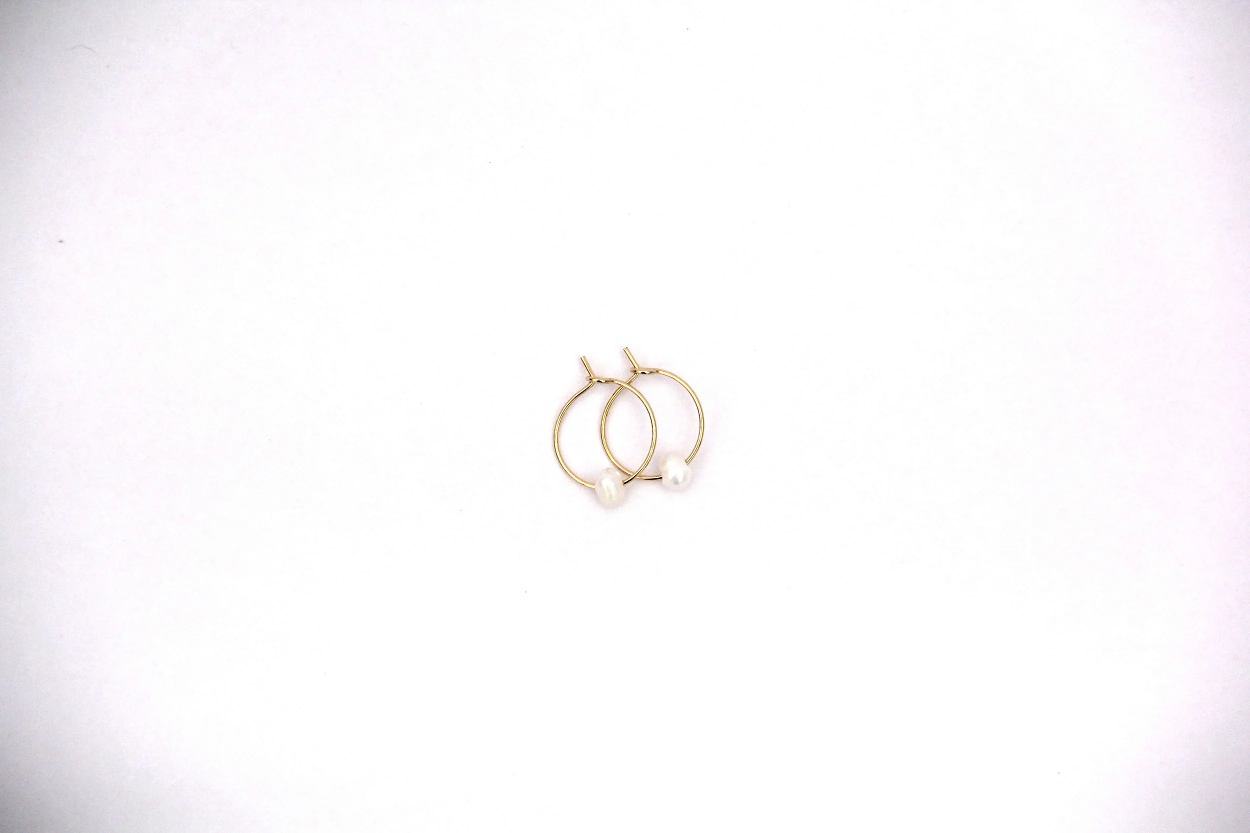 Gold stainless steel freshwater pearl hoop earrings on white background.