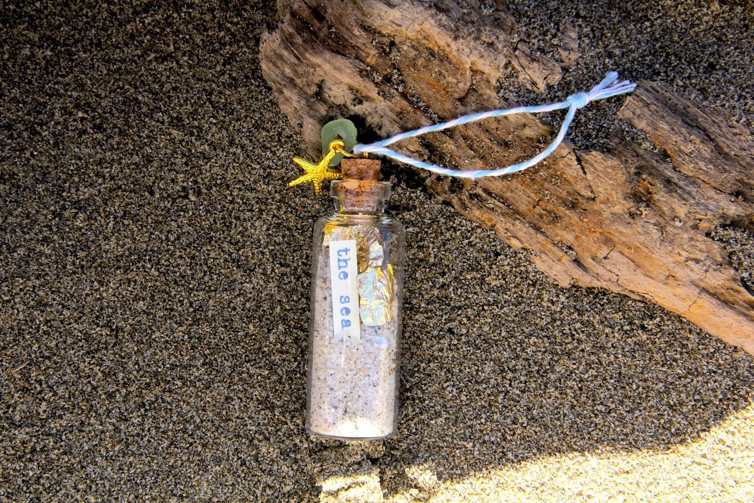 The Starfish Beach in a Bottle Ornament sitting in beach sand.