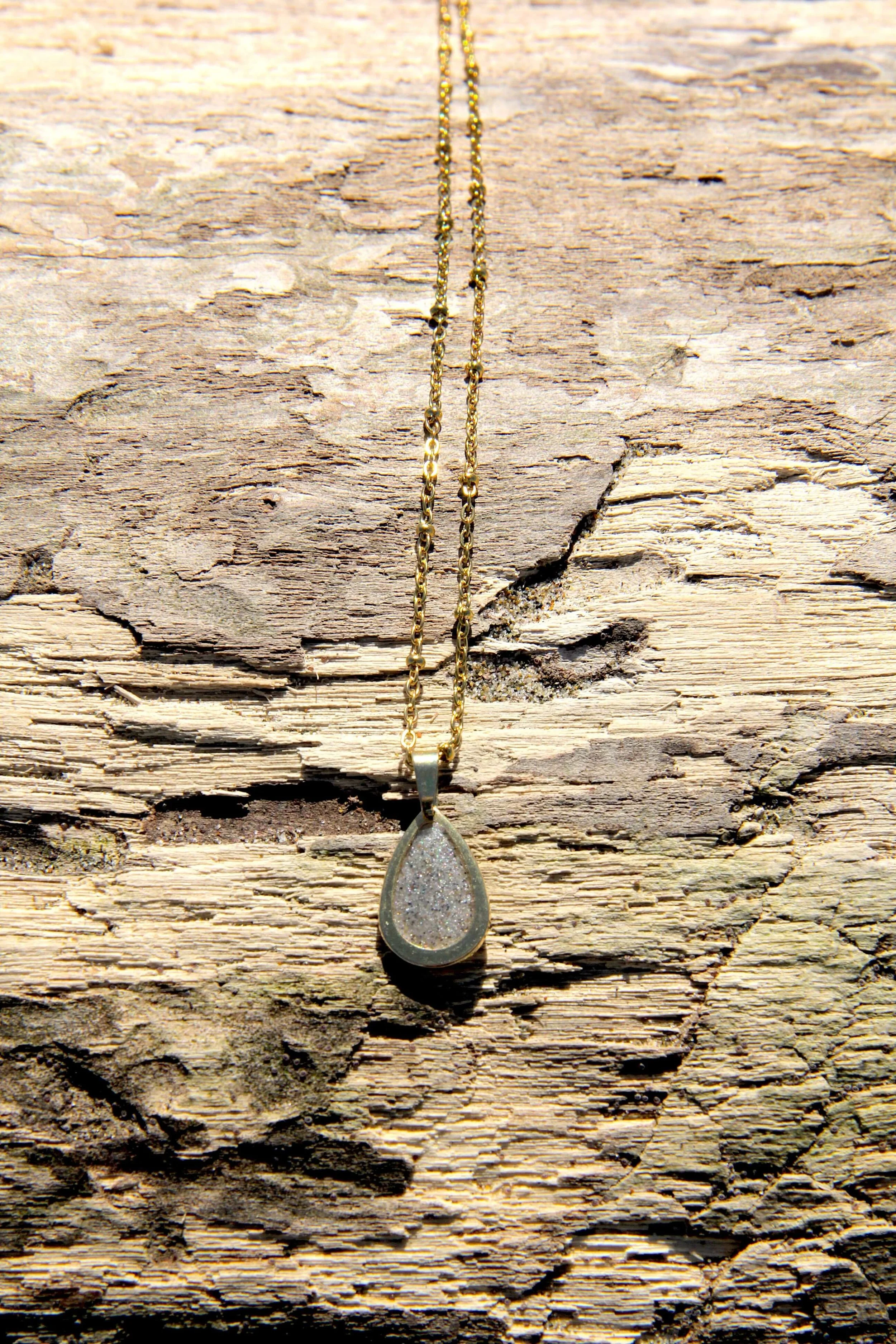 A genuine hand-collected beach sand pendant necklace laying on a driftwood log on the beach.