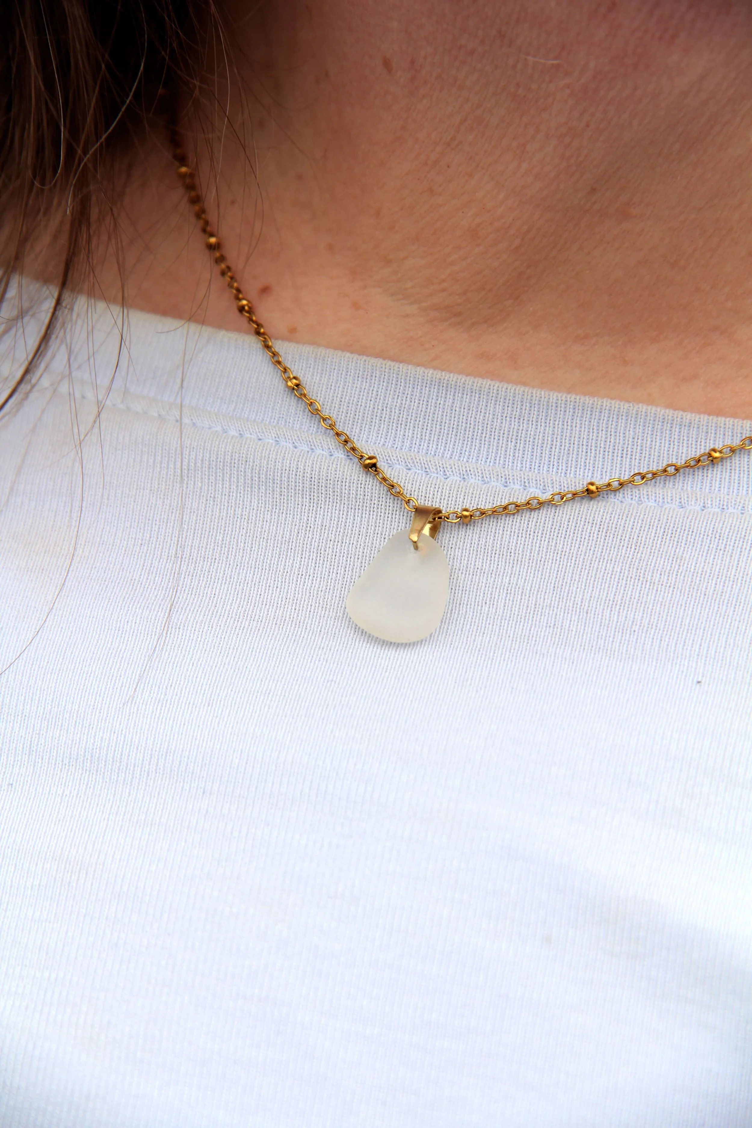A close up of a woman wearing a genuine ocean tumbled white sea glass pendant necklace around her neck.
