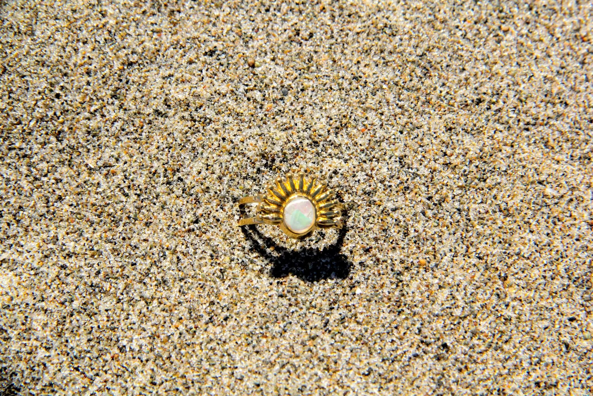 A natural iridescent abalone shell ring lying in beach sand.