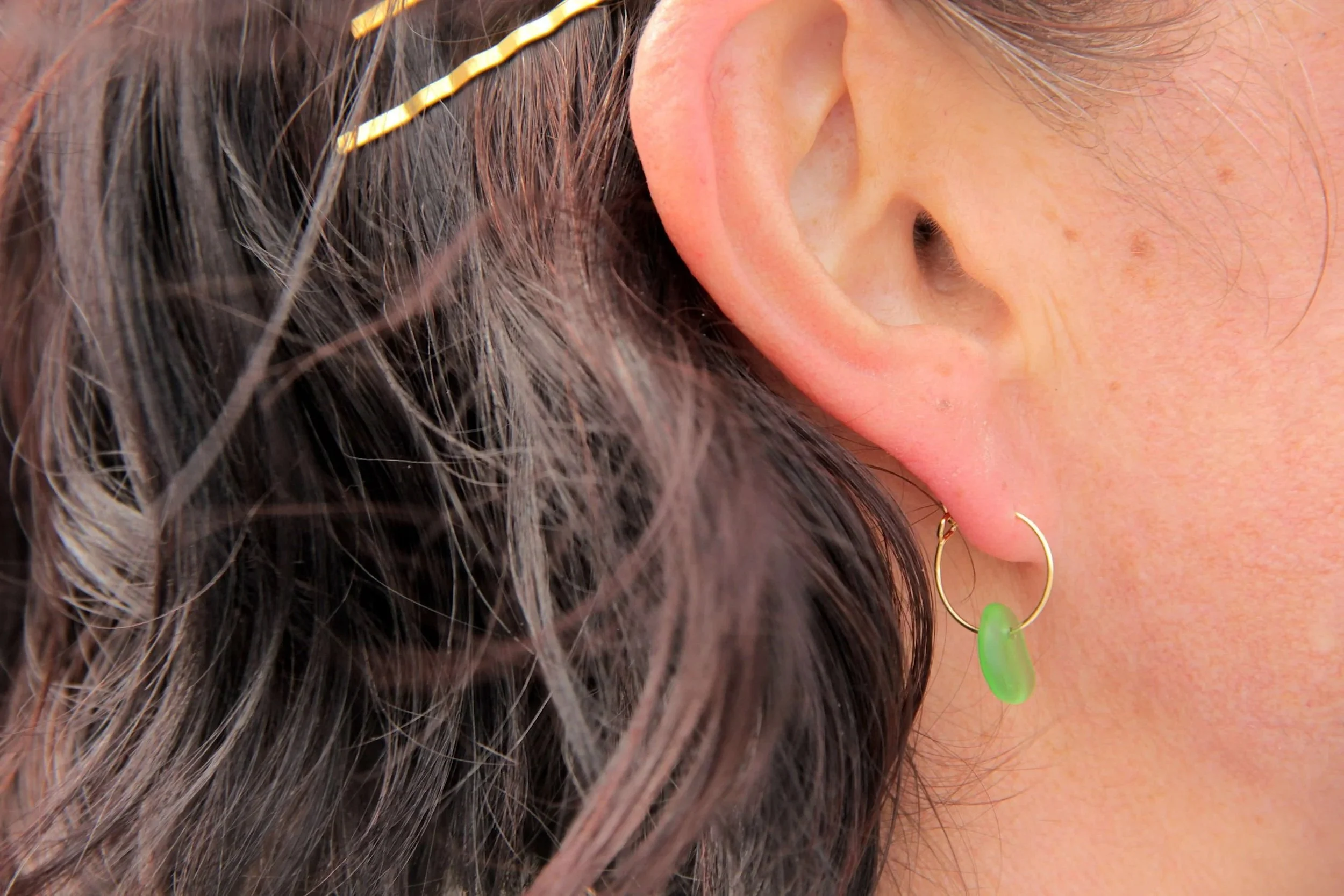 Close up of woman wearing a gold stainless steel sea glass hoop earring on her ear.