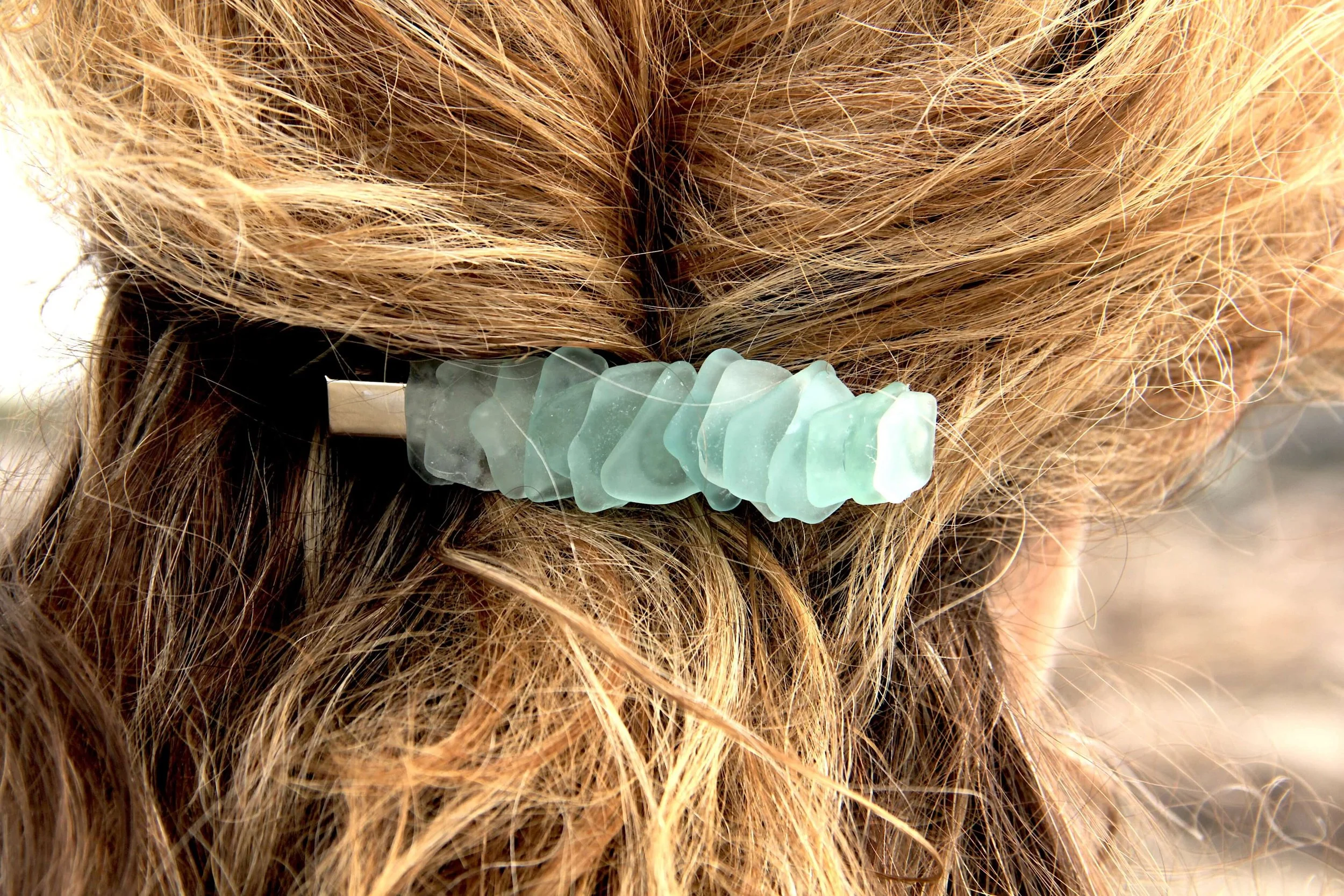 A close up of a woman wearing a blue genuine ocean tumbled sea glass hair clip in her hair.
