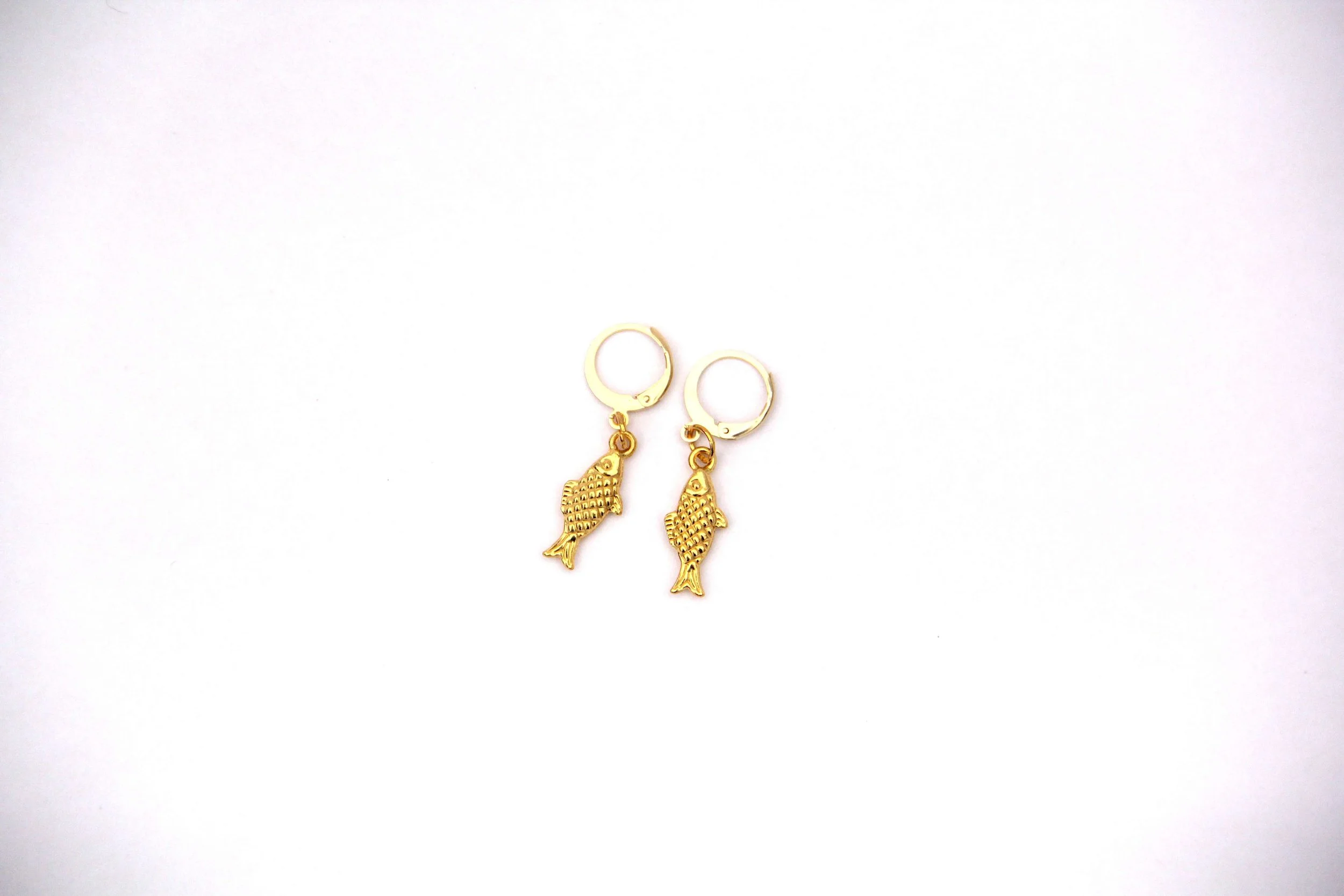A pair of gold-tone metal sardine charm huggie hoop earrings on white background.