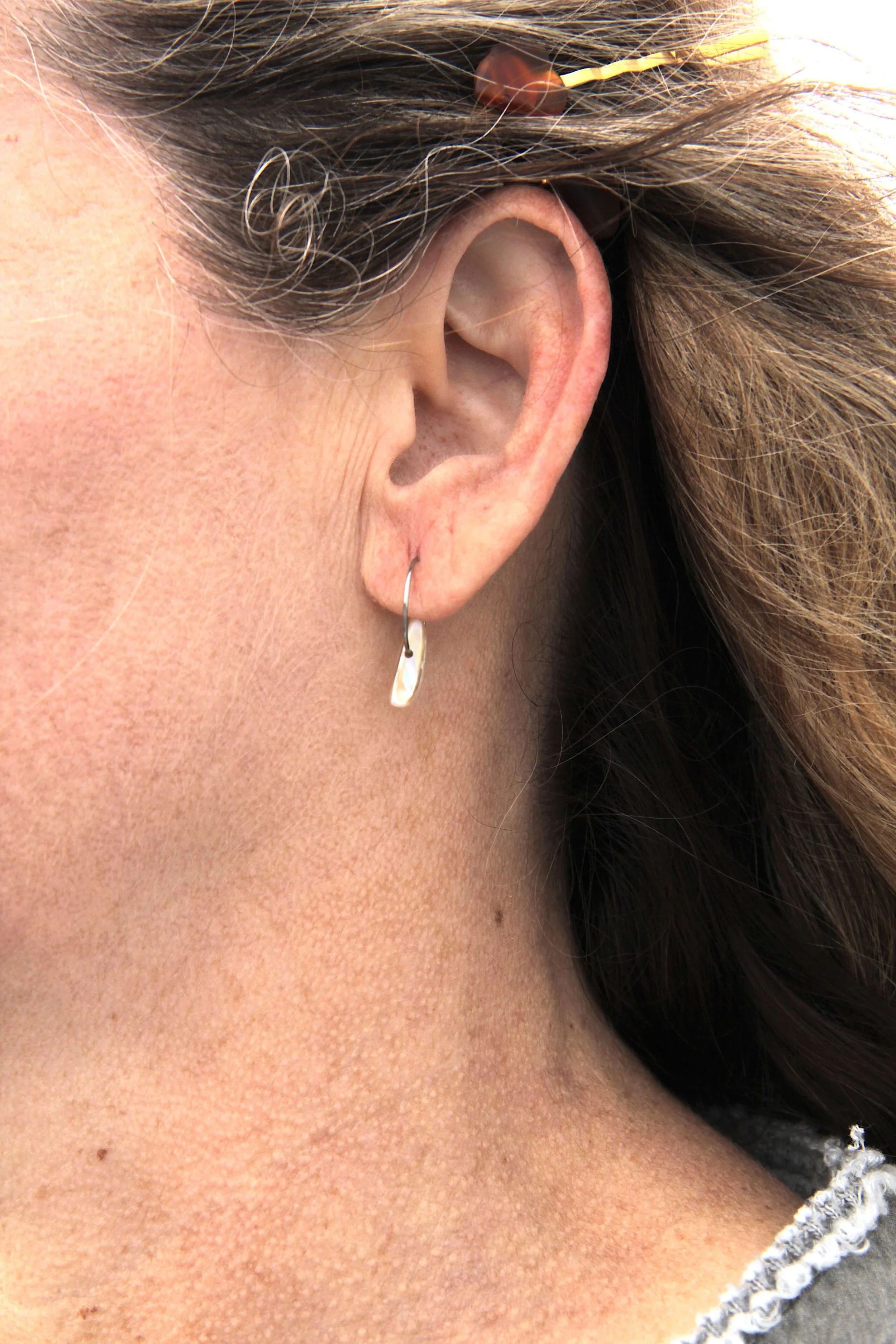 Close up of woman wearing a silver stainless steel seashell hoop earring on her ear.