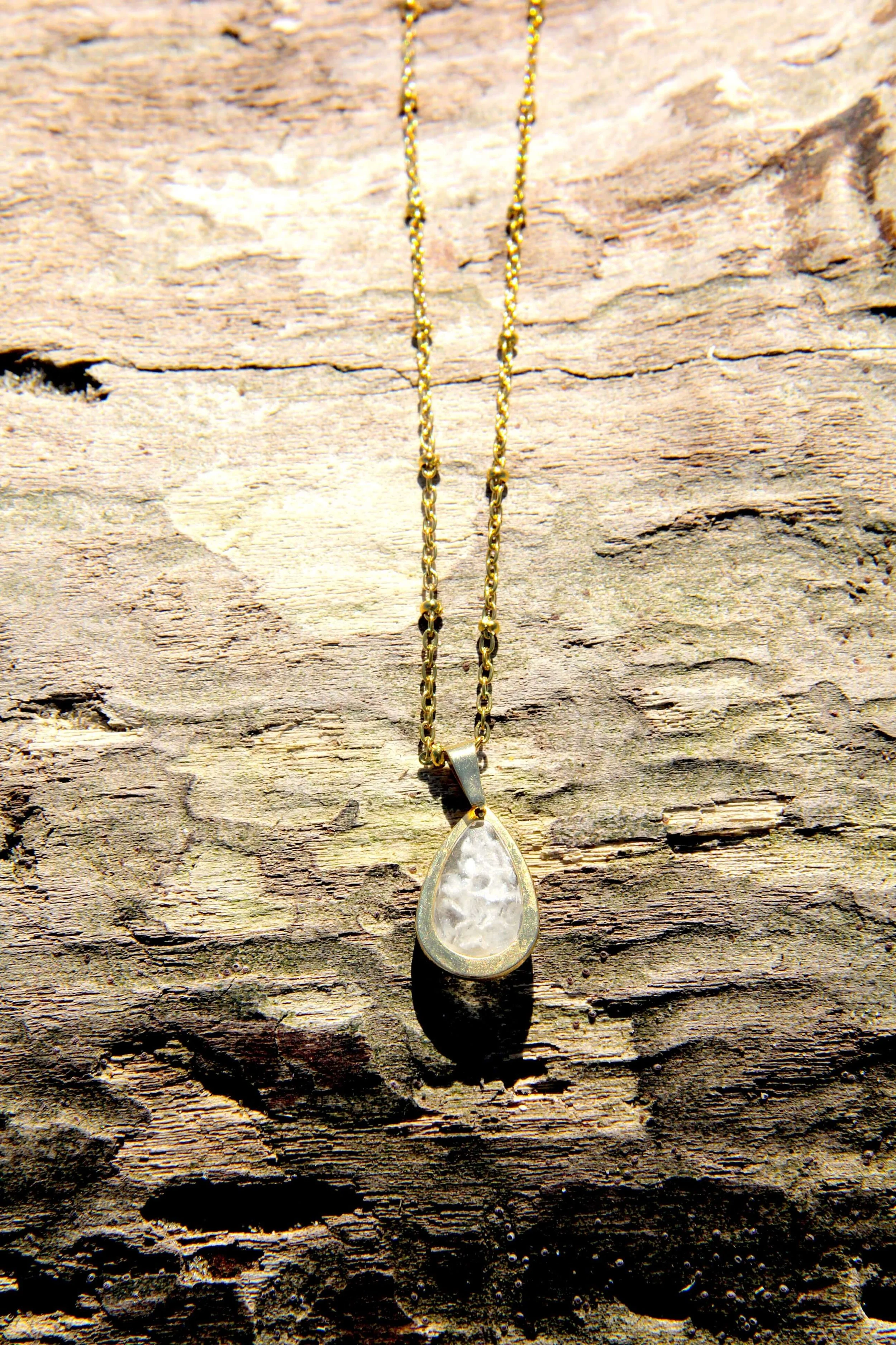 A genuine hand-collected sea salt pendant necklace laying on a driftwood log on the beach.