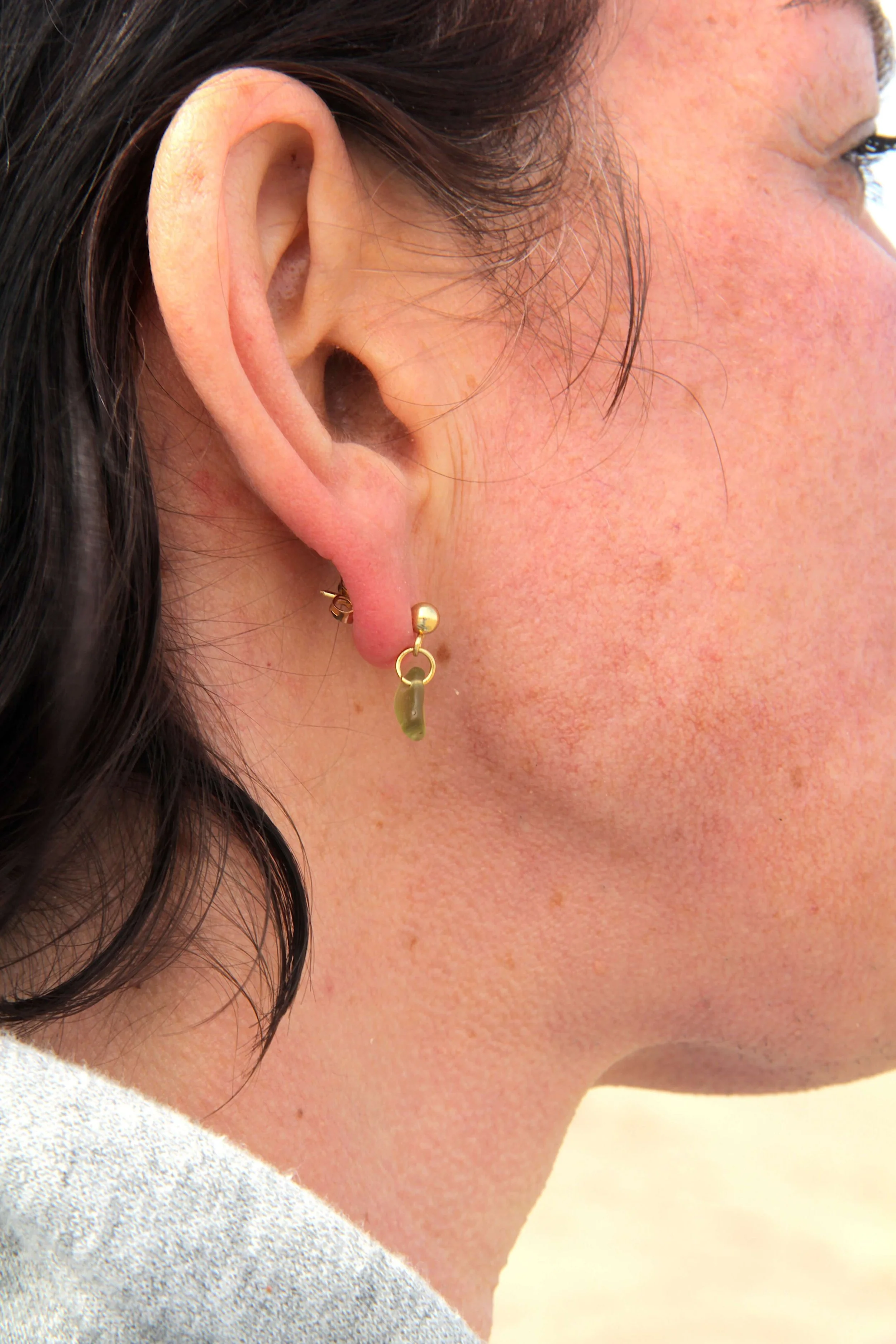 Close up of woman wearing a 18K gold-plated stainless steel green sea glass stud earring on her ear.