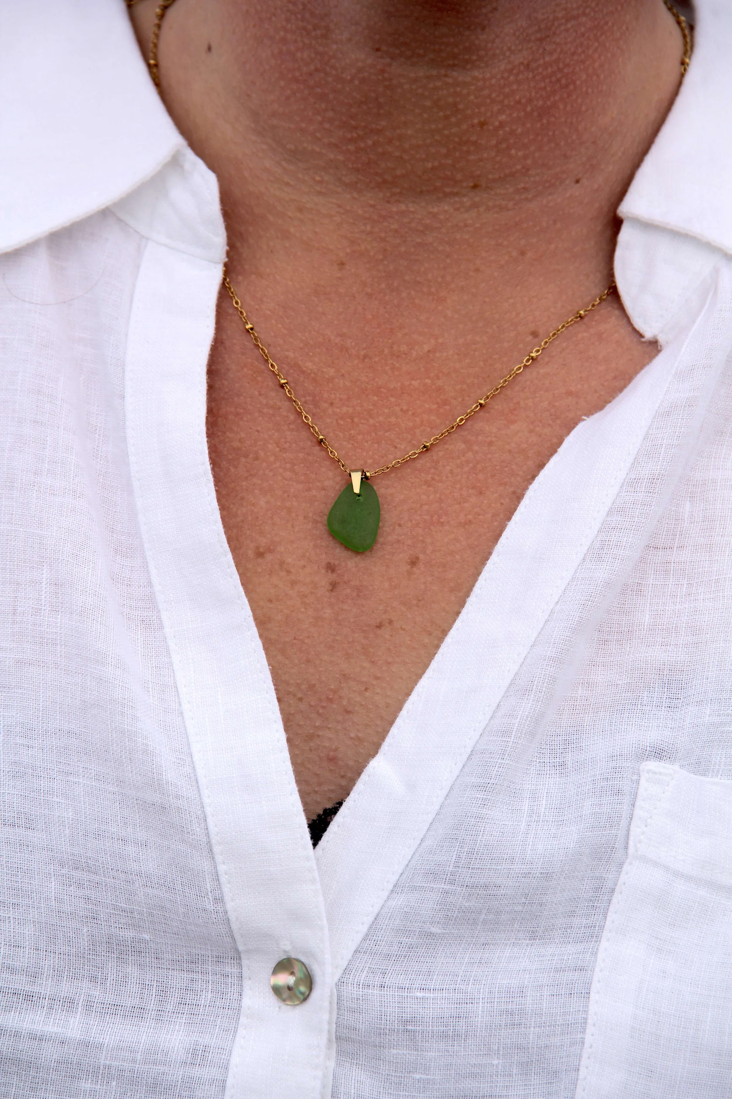 Close up of woman wearing a genuine ocean-tumbled green sea glass pendant on an 18K gold-plated stainless steel cable chain necklace.