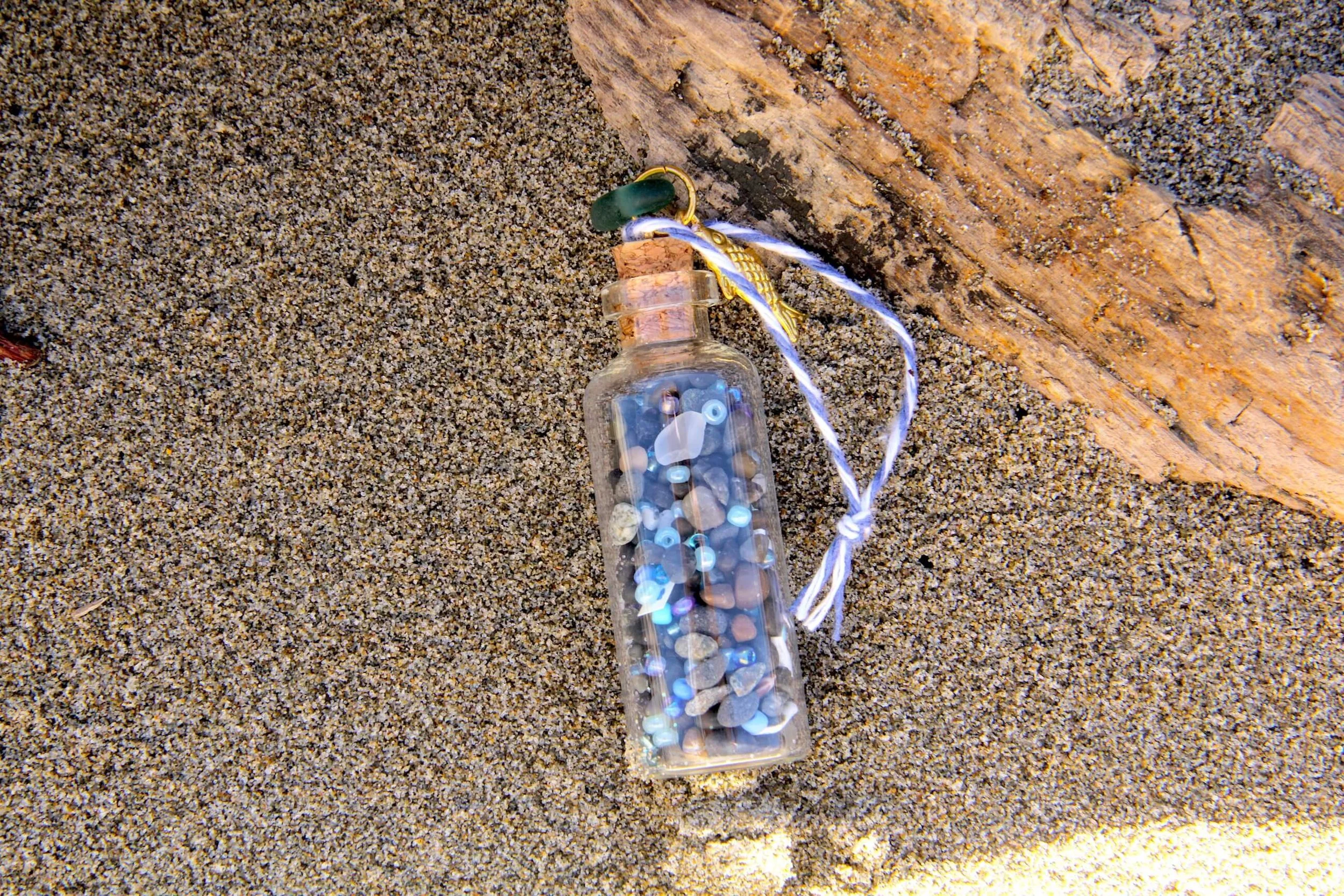 The Sardine Beach in a Bottle Ornament sitting in beach sand.