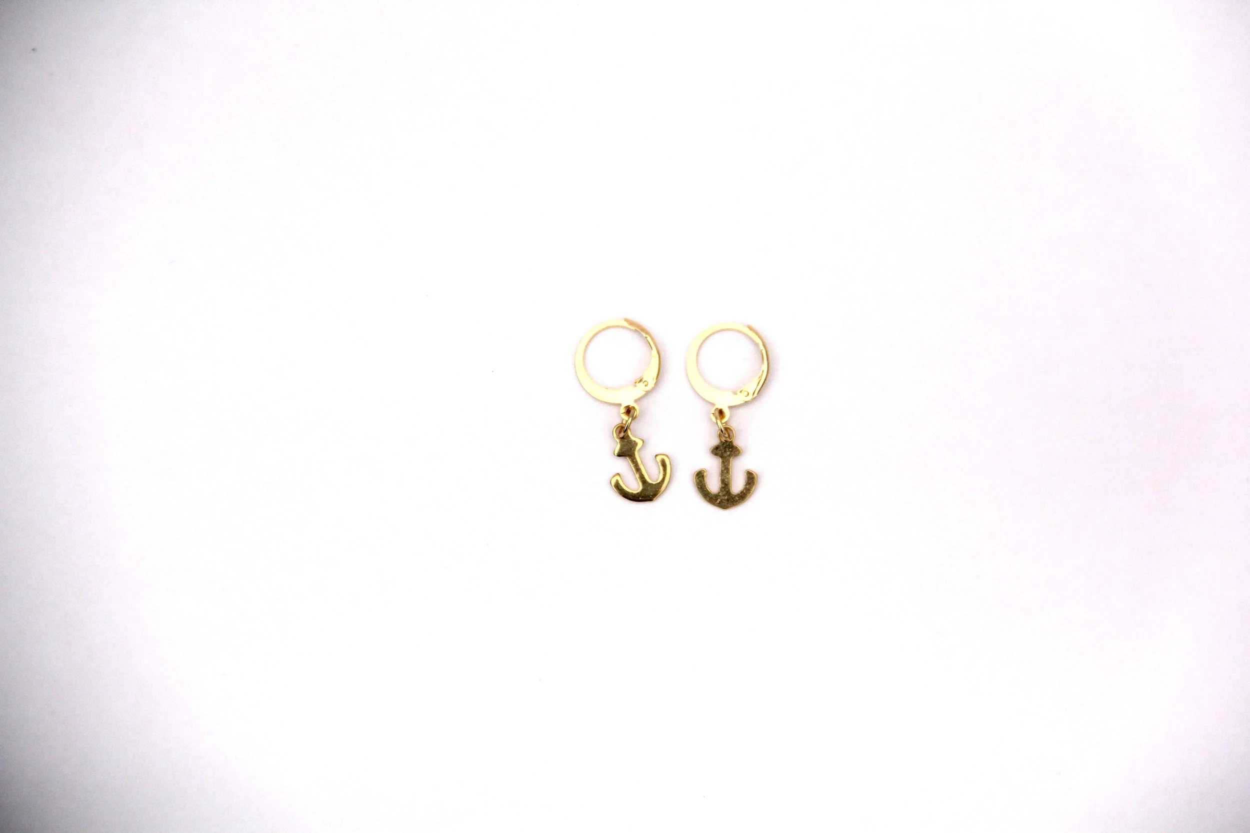 A pair of 18K gold-plated stainless steel anchor charm huggie hoop earrings on white background.