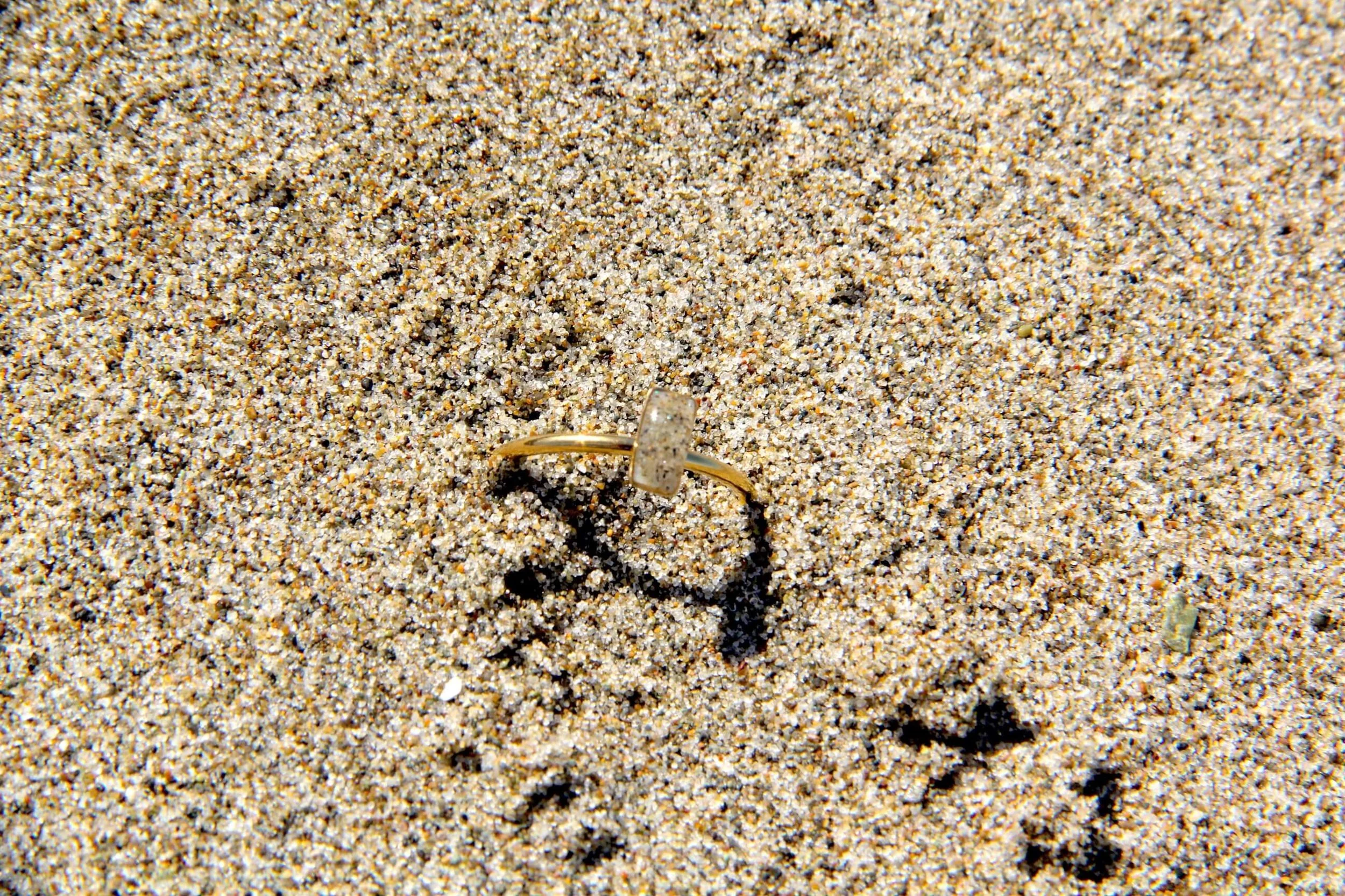 A genuine hand collected beach sand ring lying in beach sand.