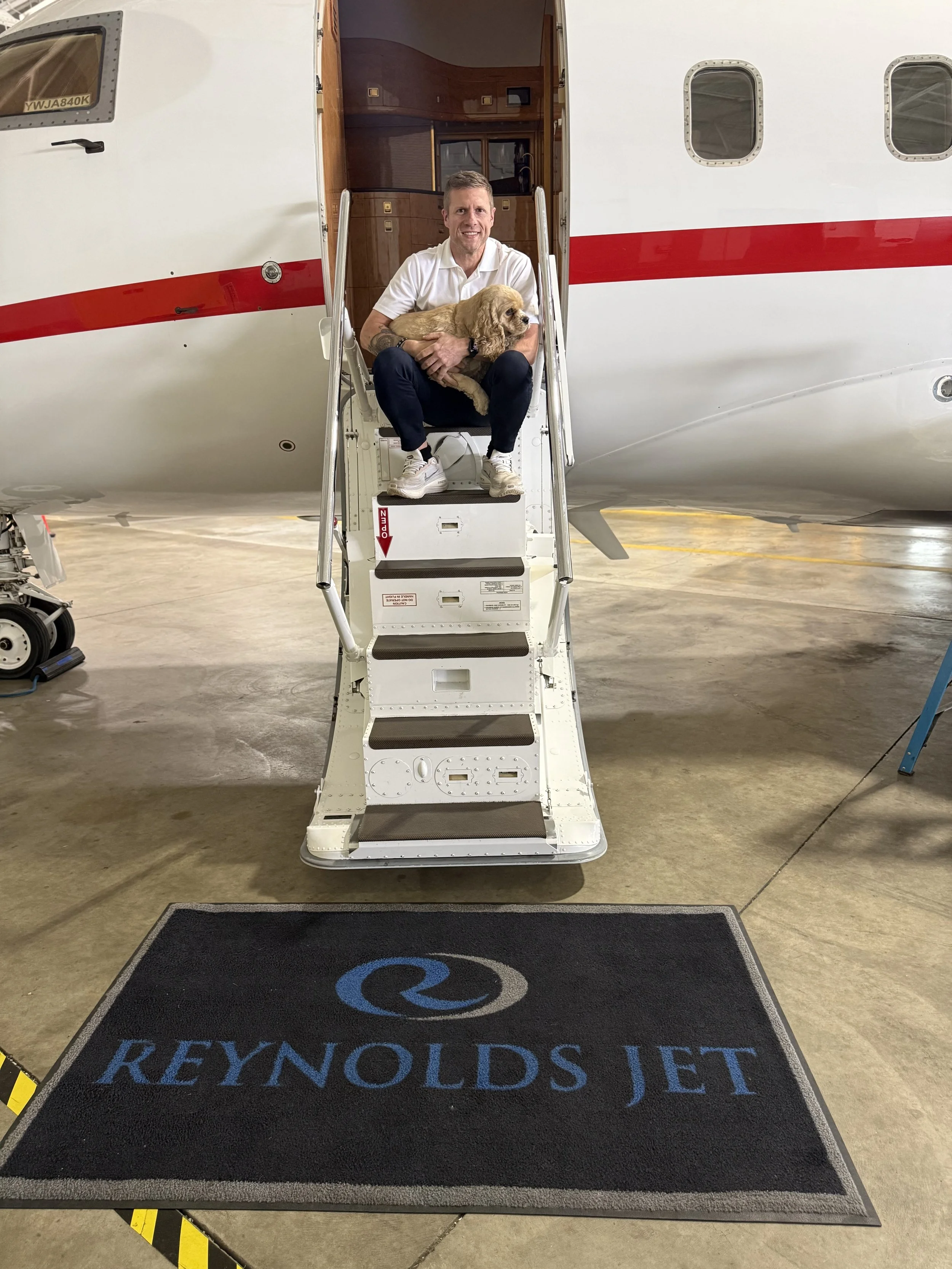 Man sitting stairs of a beautiful private aircraft  holding a cute Spaniel dog at Reynolds Jet hangar
