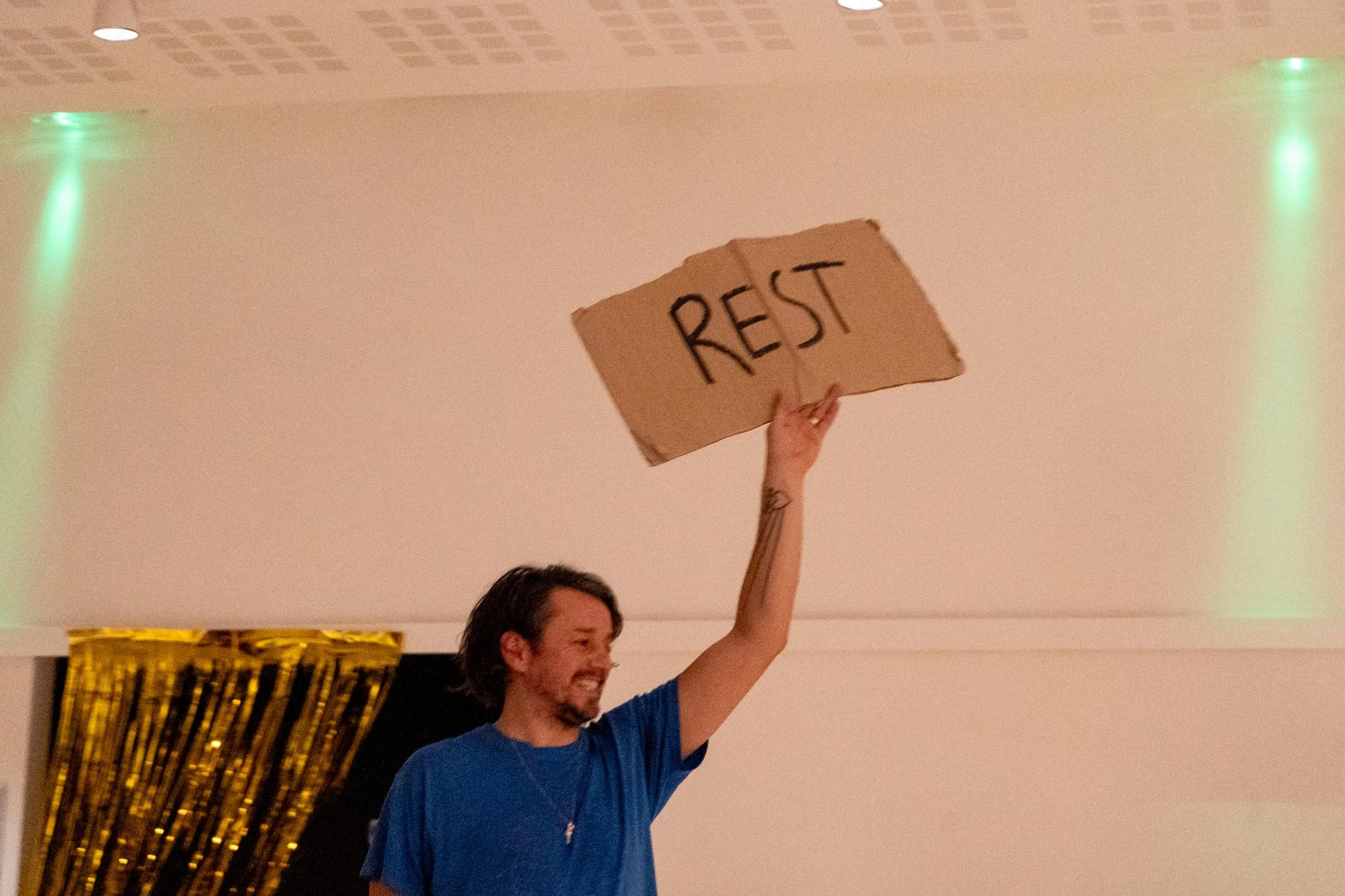 A man wearing a blue T-shirt holds up a cardboard sign that reads "Rest"