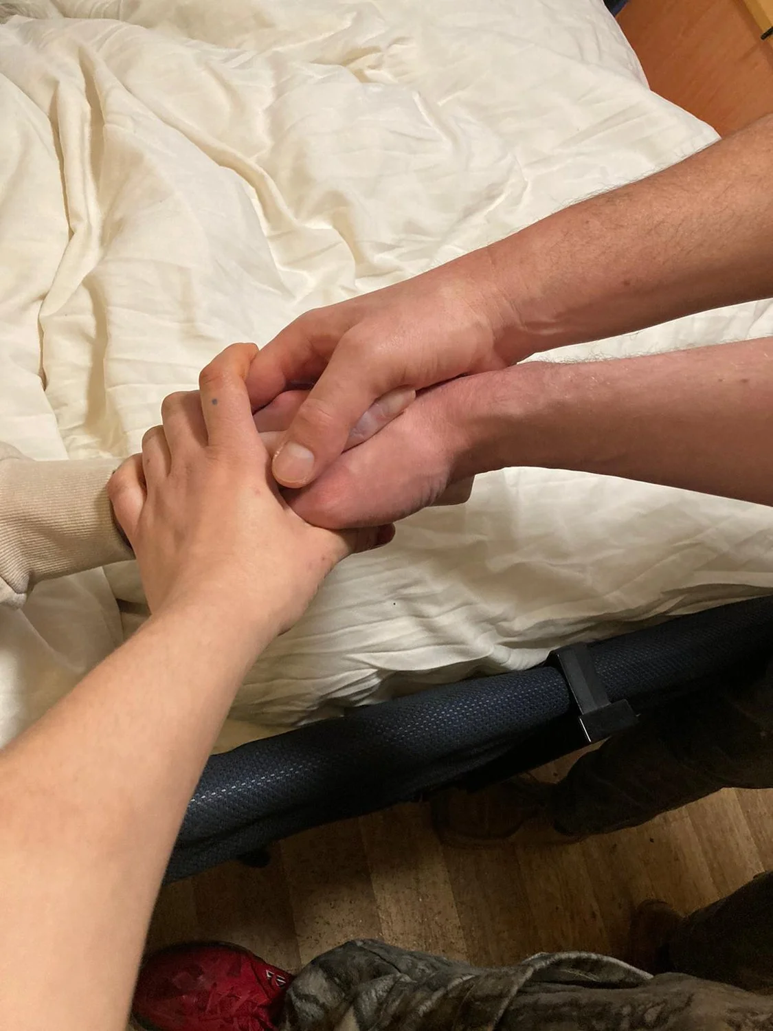 Three hands holding over a white duvet.