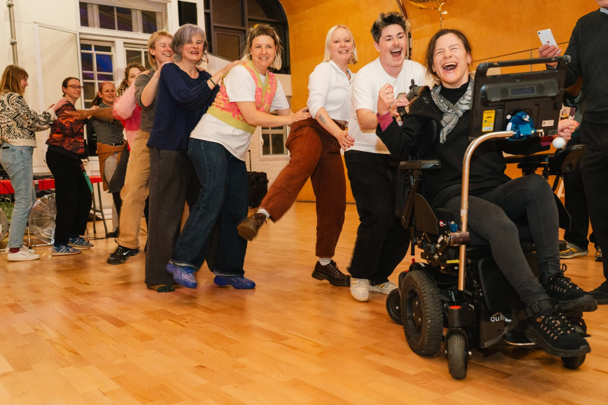 Group of people dancing in a line led by a woman in a wheelchair
