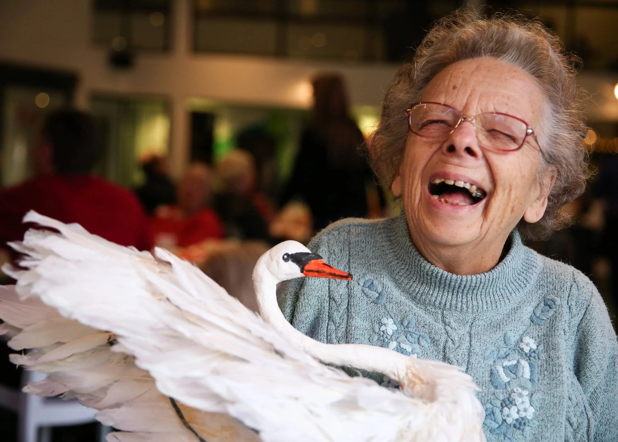 An older woman laughing whilst holding a swan she has made from papermache