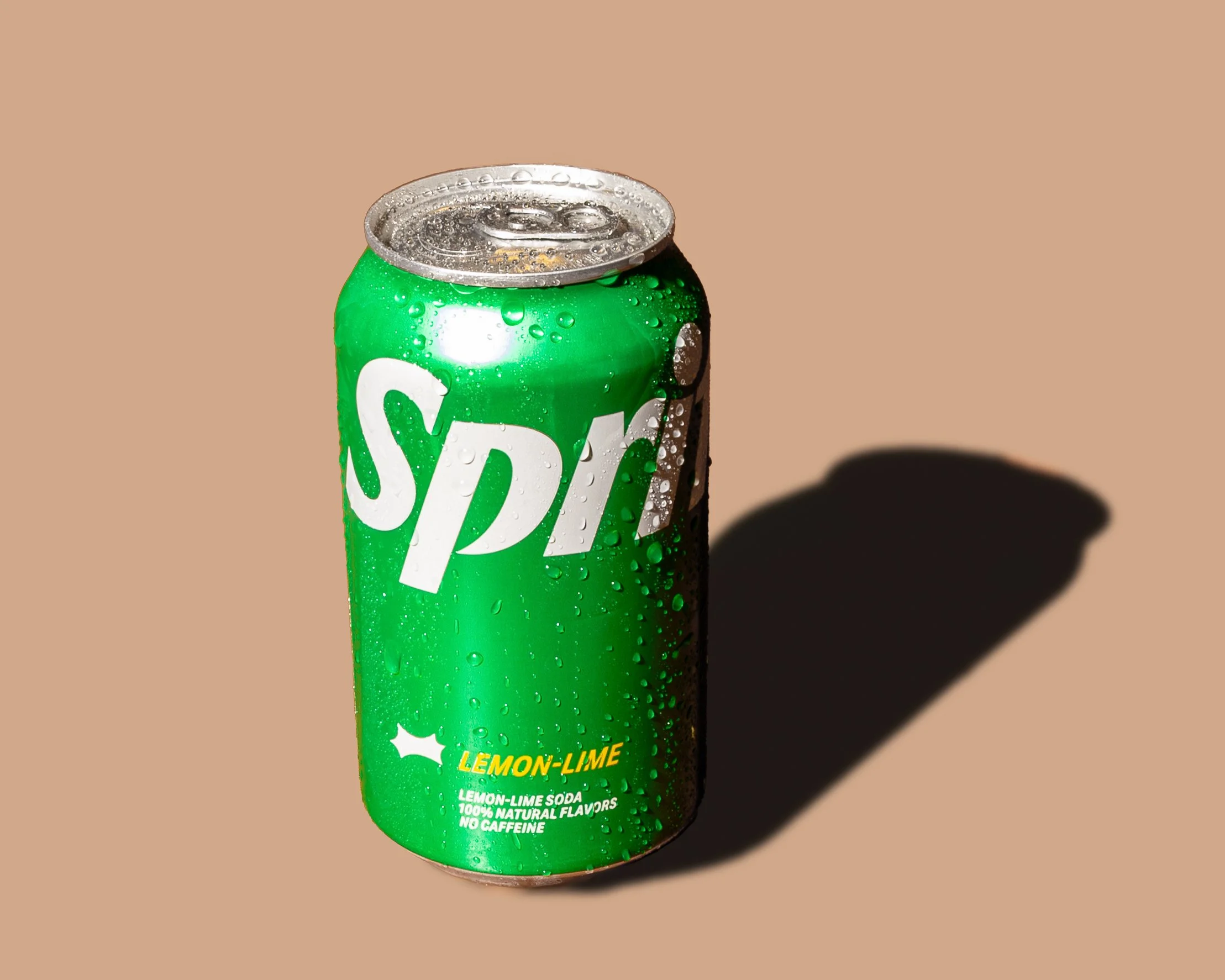 Can of Sprite Lemon-Lime soda with condensation and bubbles, featuring a green label and a silver top, casting a shadow on a light brown background.