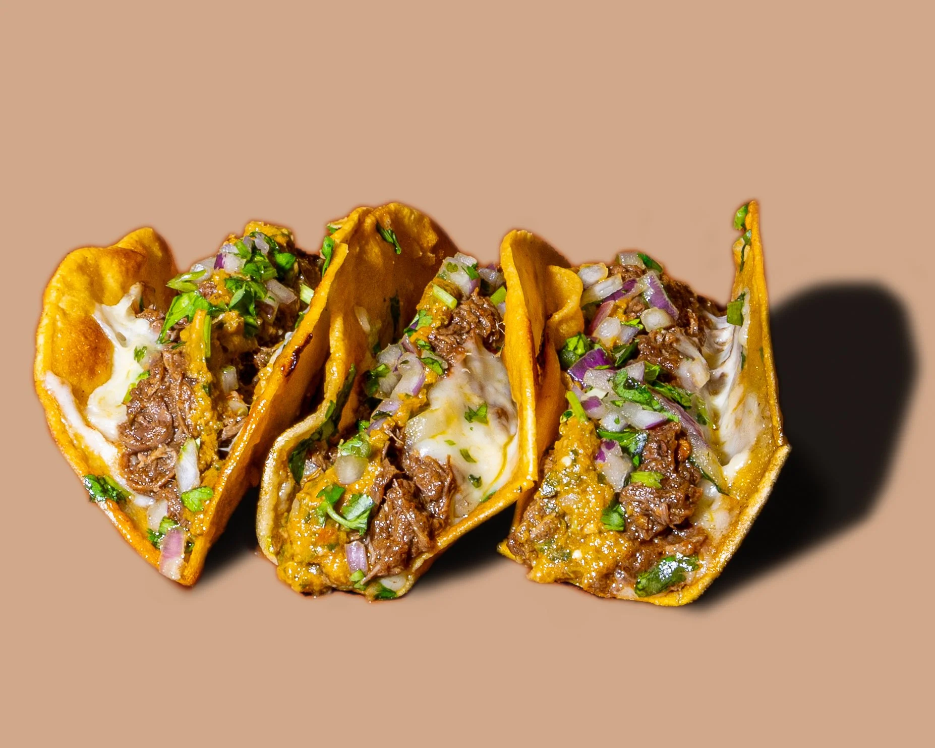 Four tacos filled with seasoned beef, melted cheese, chopped onions, and cilantro.