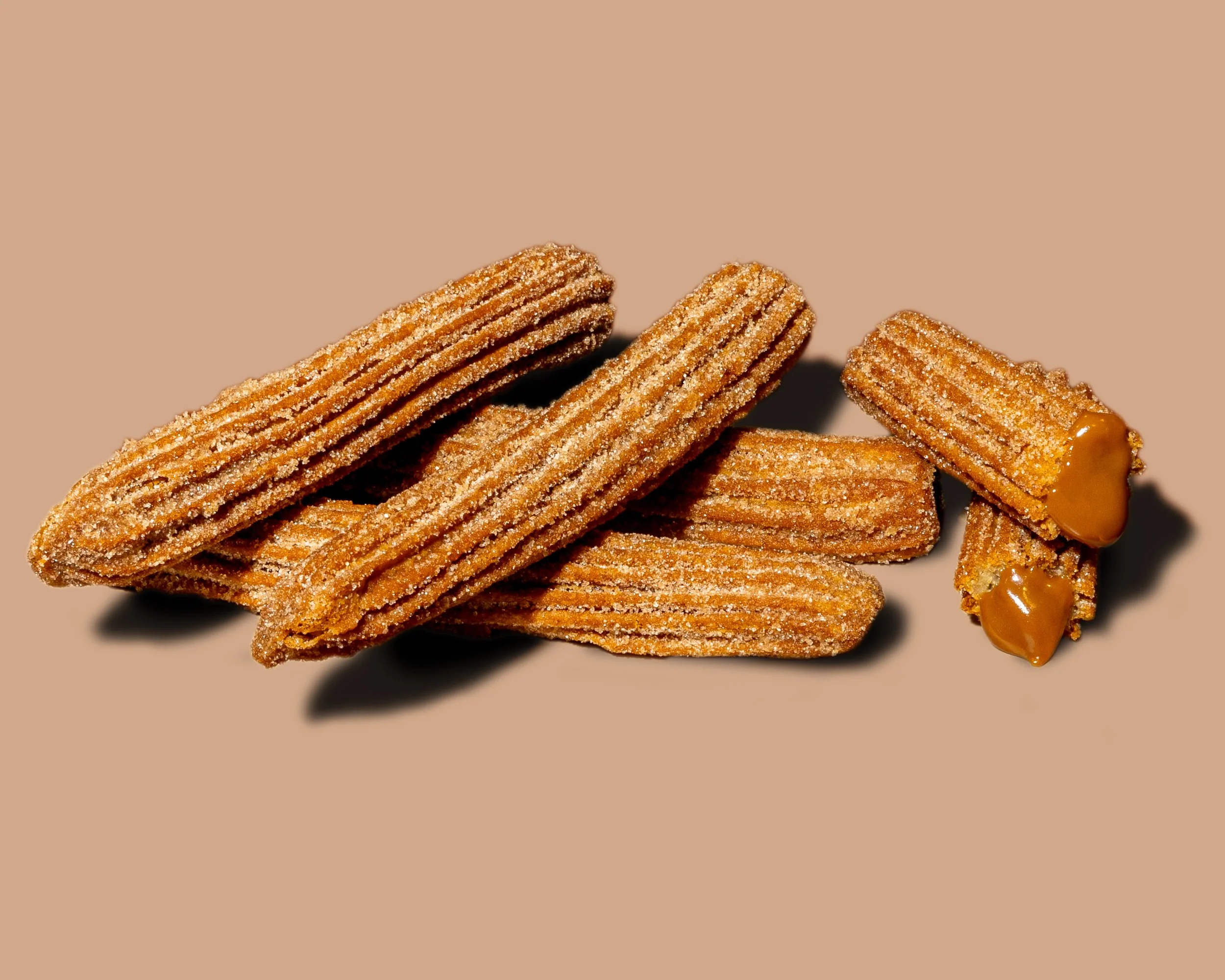 Several churros covered in cinnamon sugar stacked on top of each other, with a caramel sauce on the side.