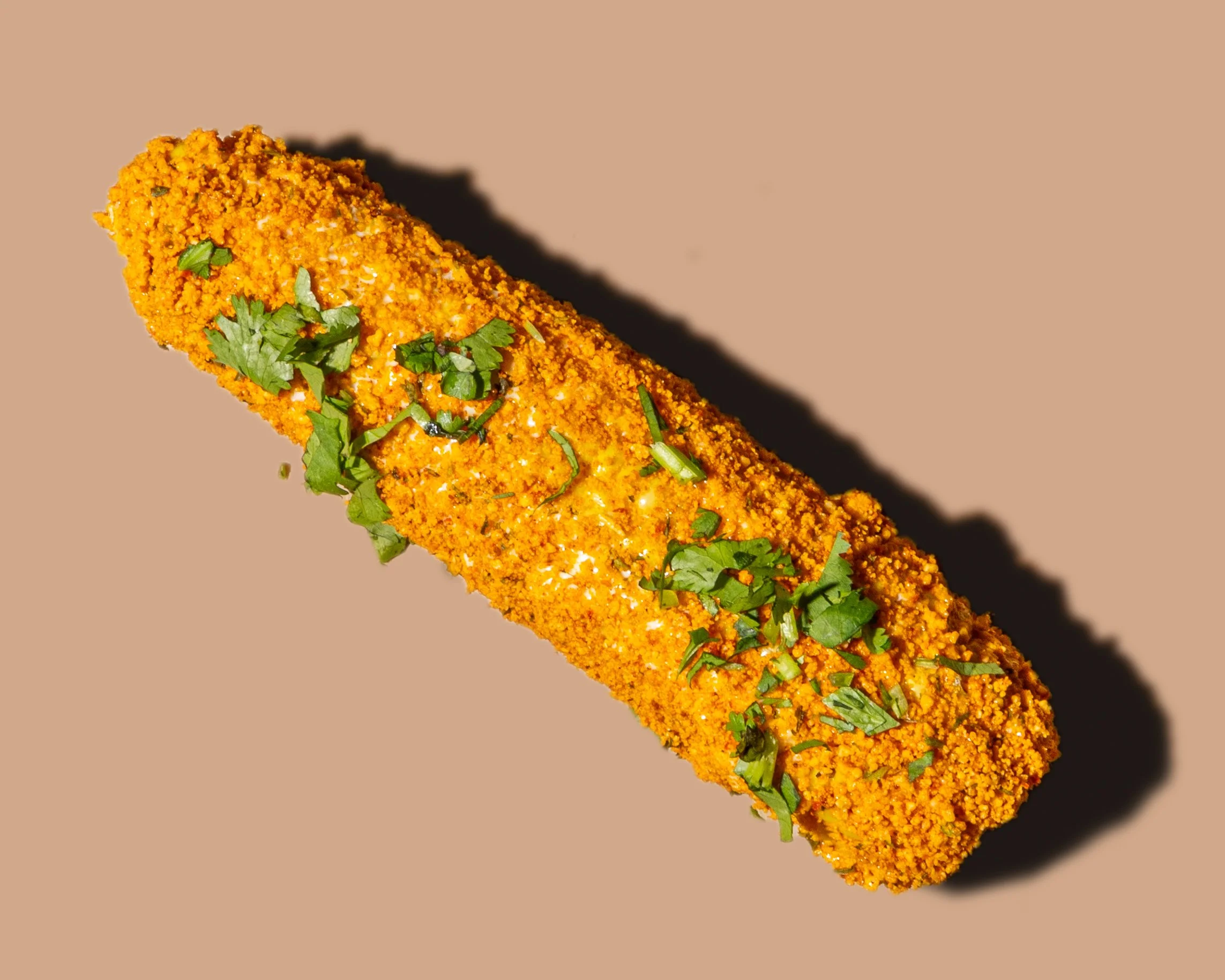A close-up of a breaded fish fillet topped with chopped herbs on a beige background.