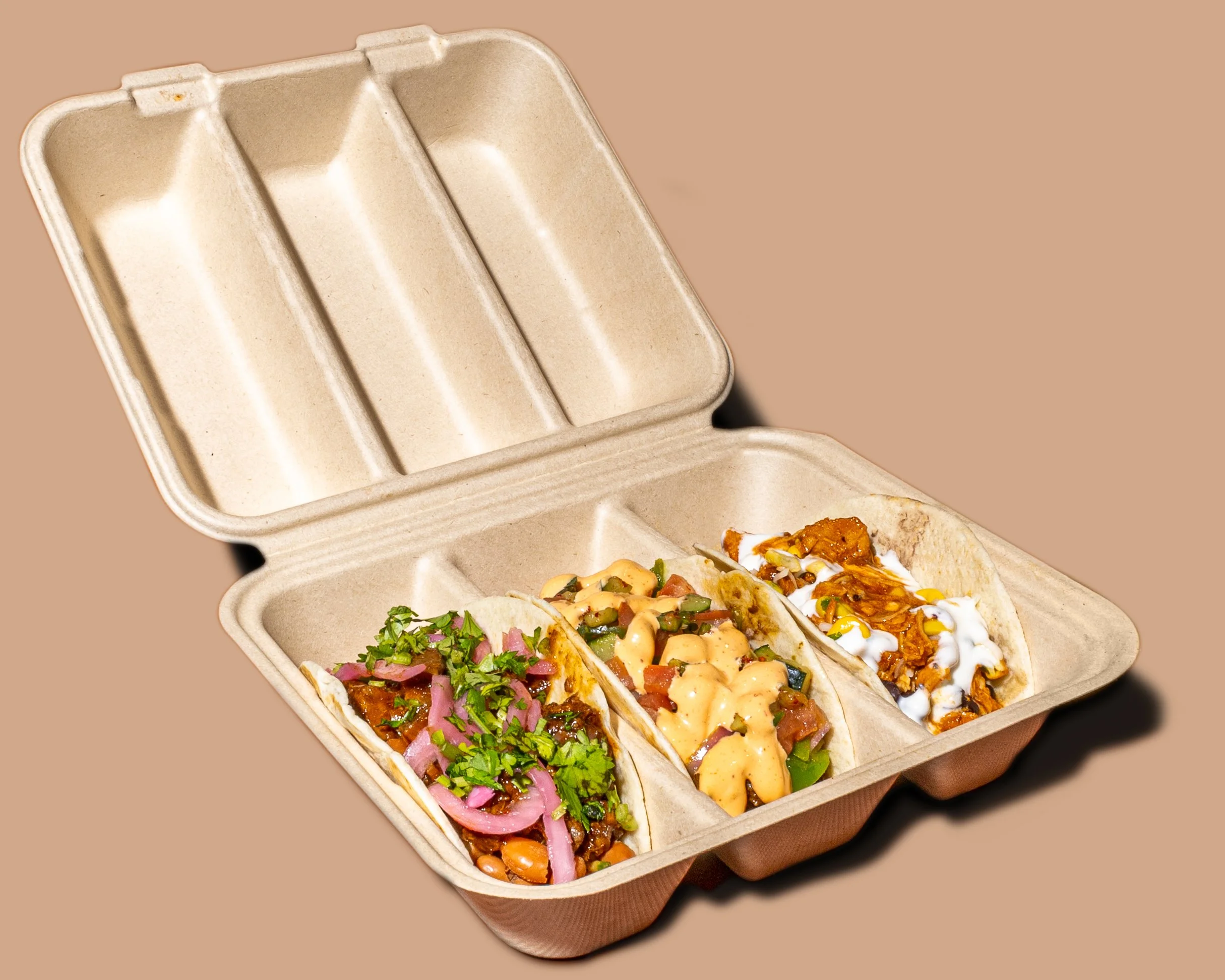 Three tacos filled with meat, onions, cilantro, cheese, and sauce, in a cardboard takeout container.