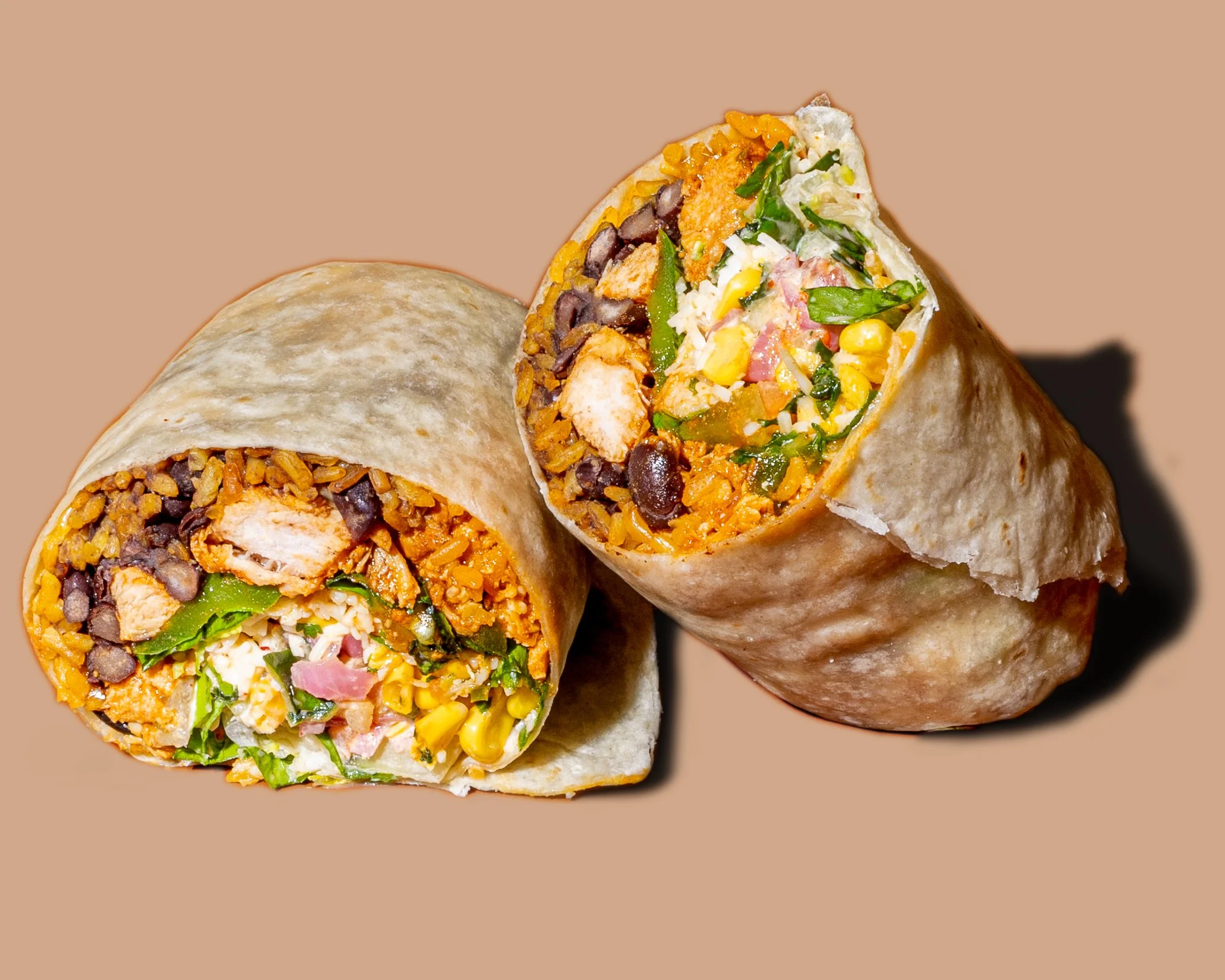 Close-up of a burrito cut in half, showing rice, black beans, grilled chicken, corn, lettuce, and other vegetables inside a flour tortilla.