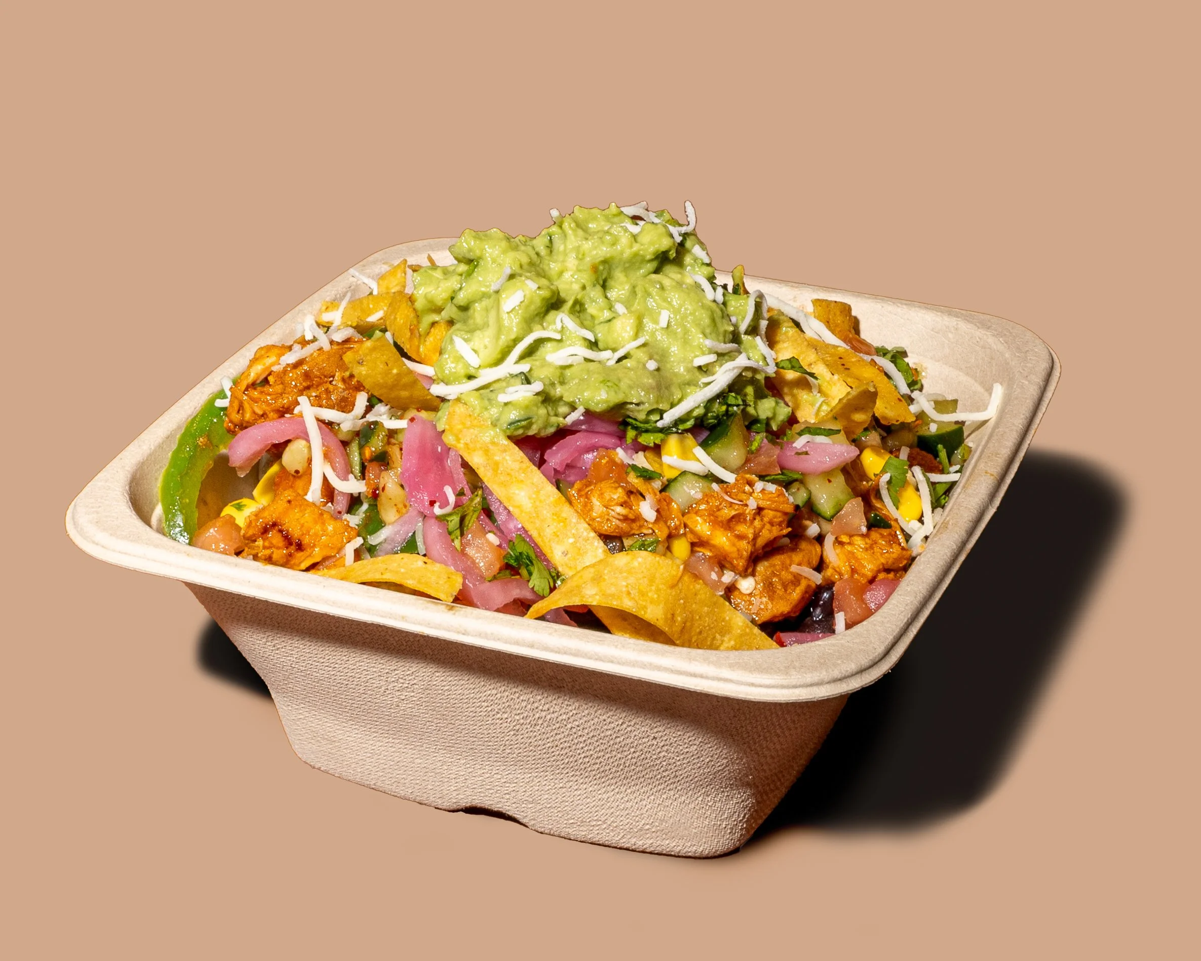A cardboard tray of loaded nachos topped with guacamole, shredded cheese, sliced pickled onions, chopped cilantro, and melted cheese.