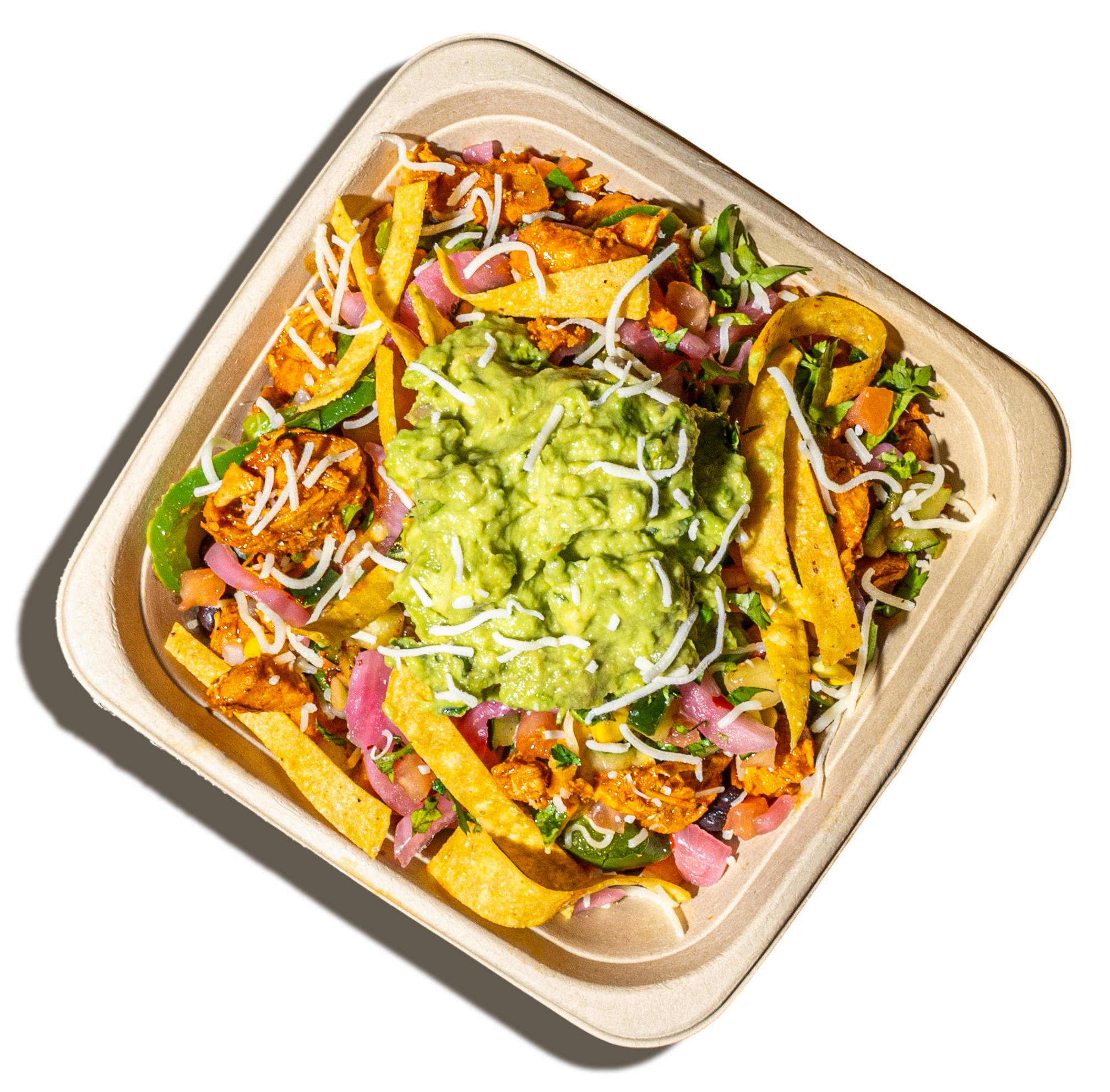 A takeout container filled with various Mexican food ingredients including guacamole, shredded cheese, taco shells, chopped vegetables, and cooked seasoned meat.