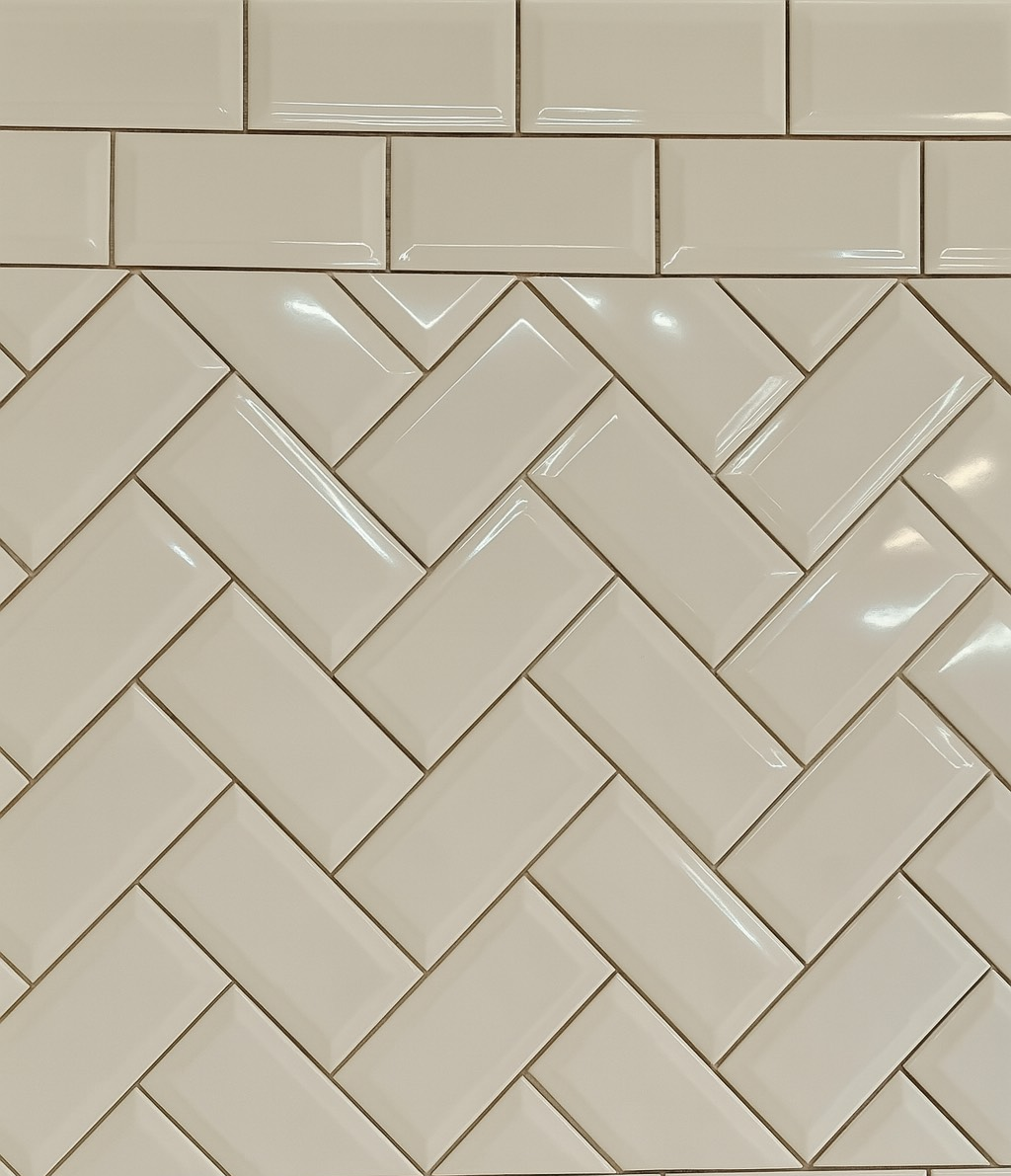 White ceramic tiles arranged in a herringbone pattern with some rectangular tiles at the top.