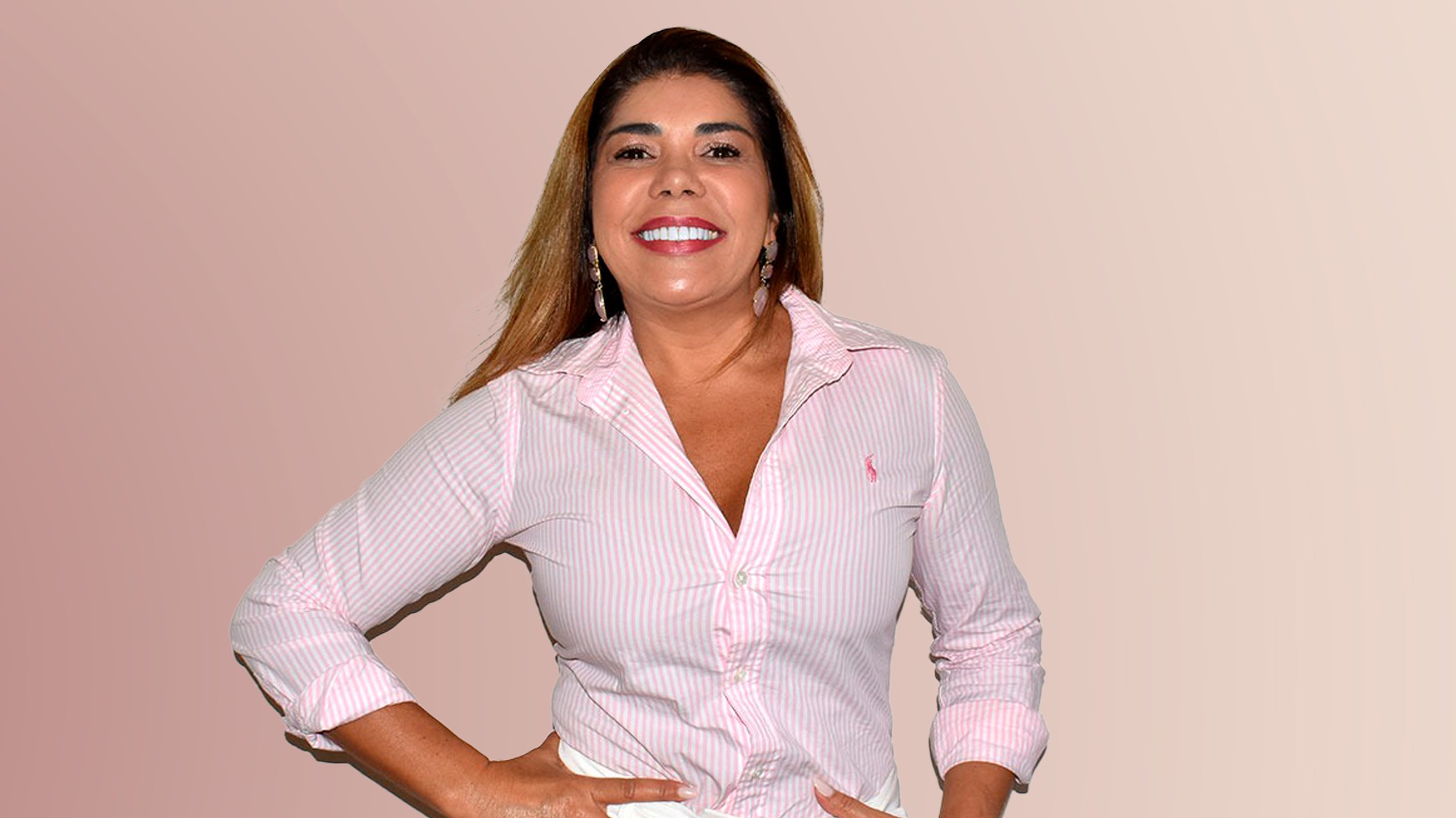 Mulher sorridente com cabelo castanho claro, usando camisa rosa de botão, de braço na cintura, contra fundo branco.