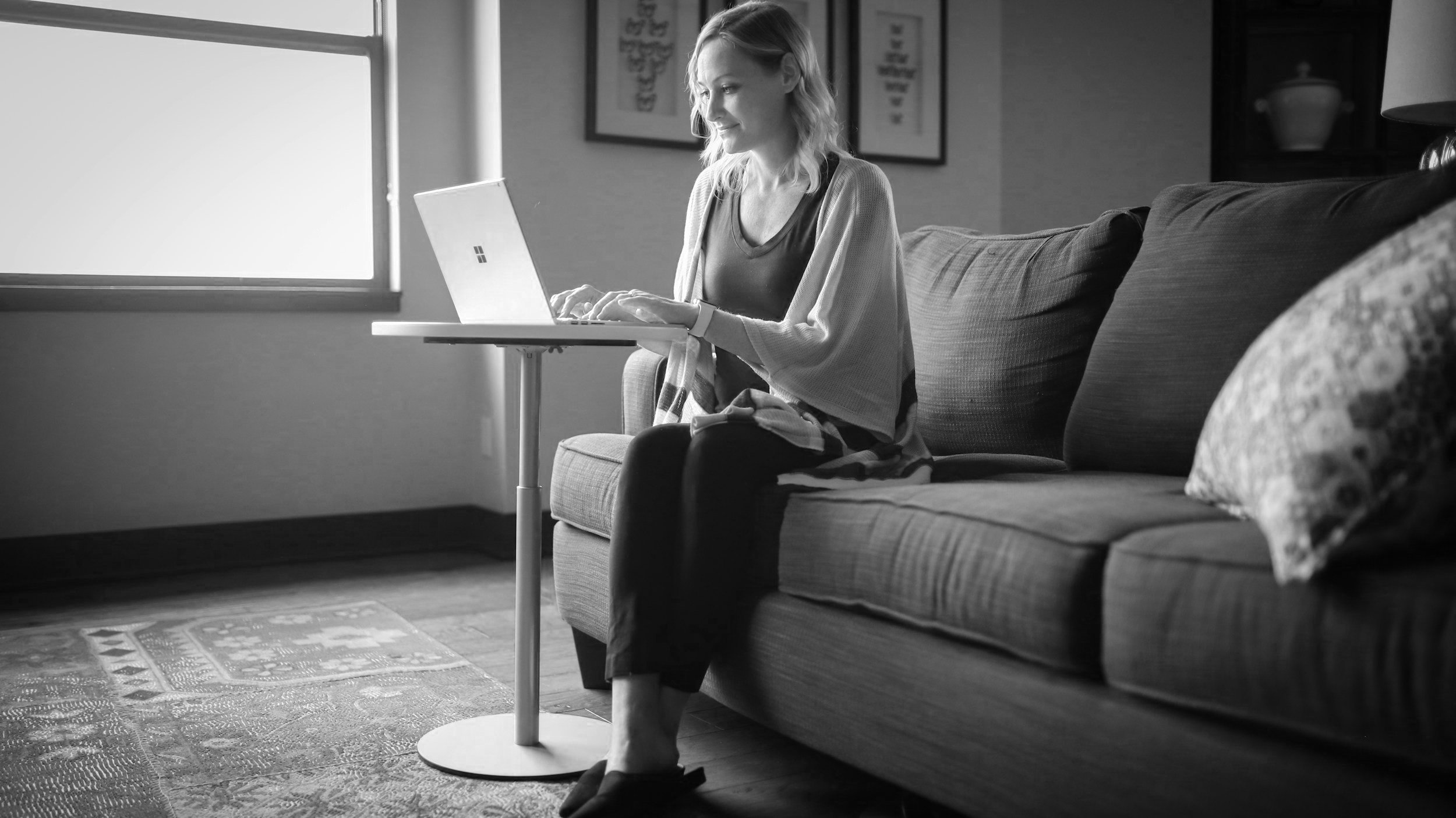 terapia individual online, psicologa debora teodora. Mulher sentada no sofá usando um laptop perto de uma janela com luz natural, ambiente doméstico.
