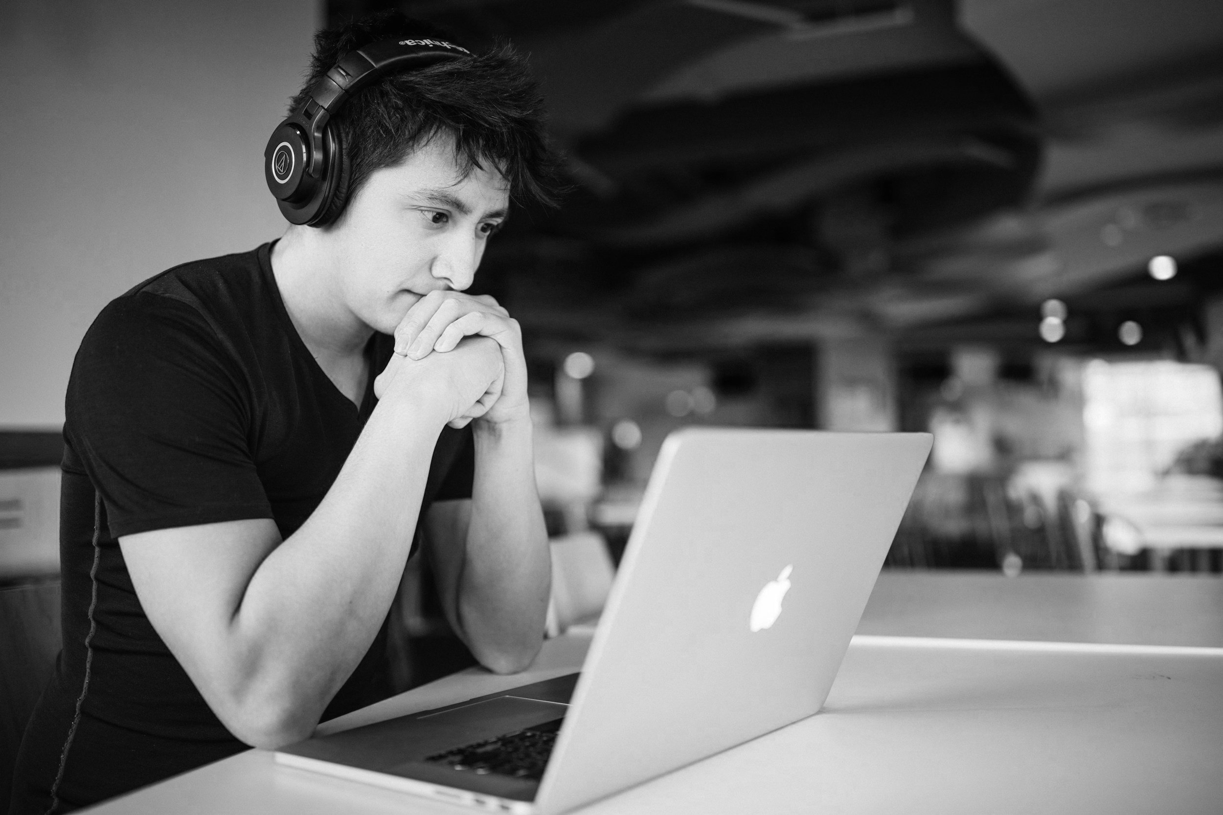 Jovem observando atentamente uma tela de laptop enquanto usa fones de ouvido em um ambiente interno
