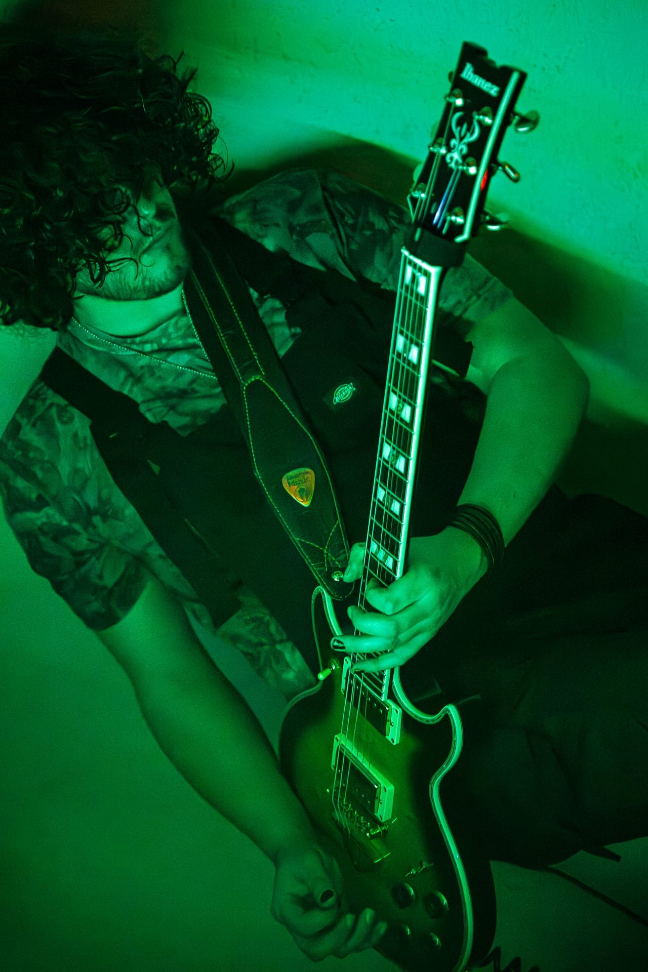 Urs mit dunklen, lockigen Haaren spielt elektrische Gitarre in einem Raum mit grüner Beleuchtung.