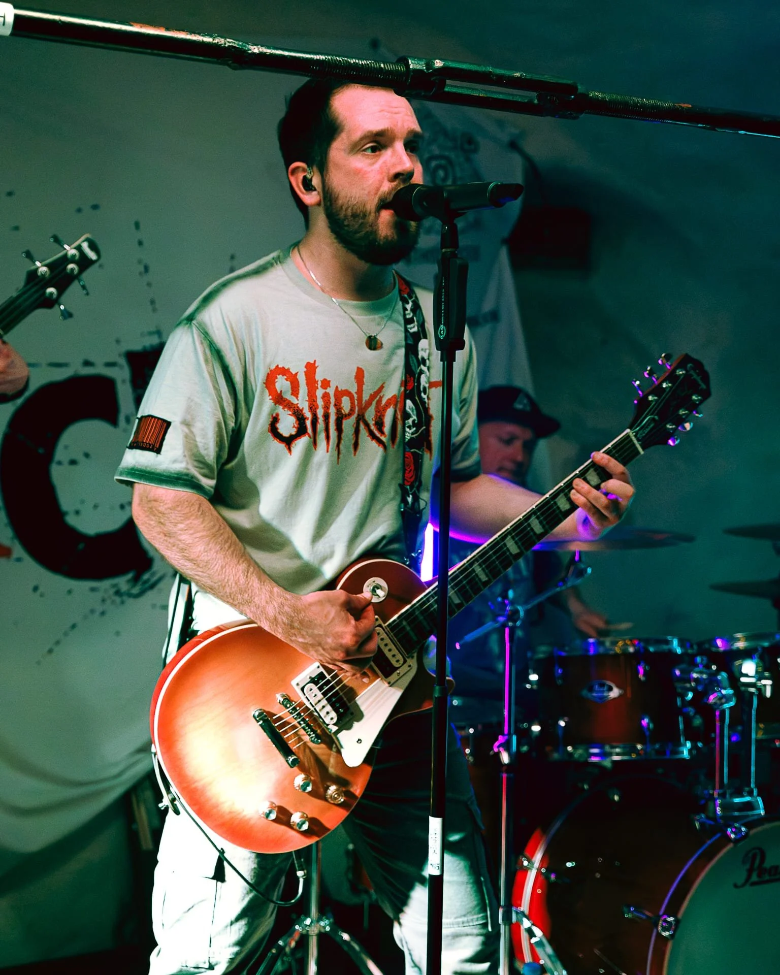 Niklas spielt E-Gitarre während eines Live-Auftritts. Er trägt ein Slipknot-T-Shirt und singt in ein Mikrofon.