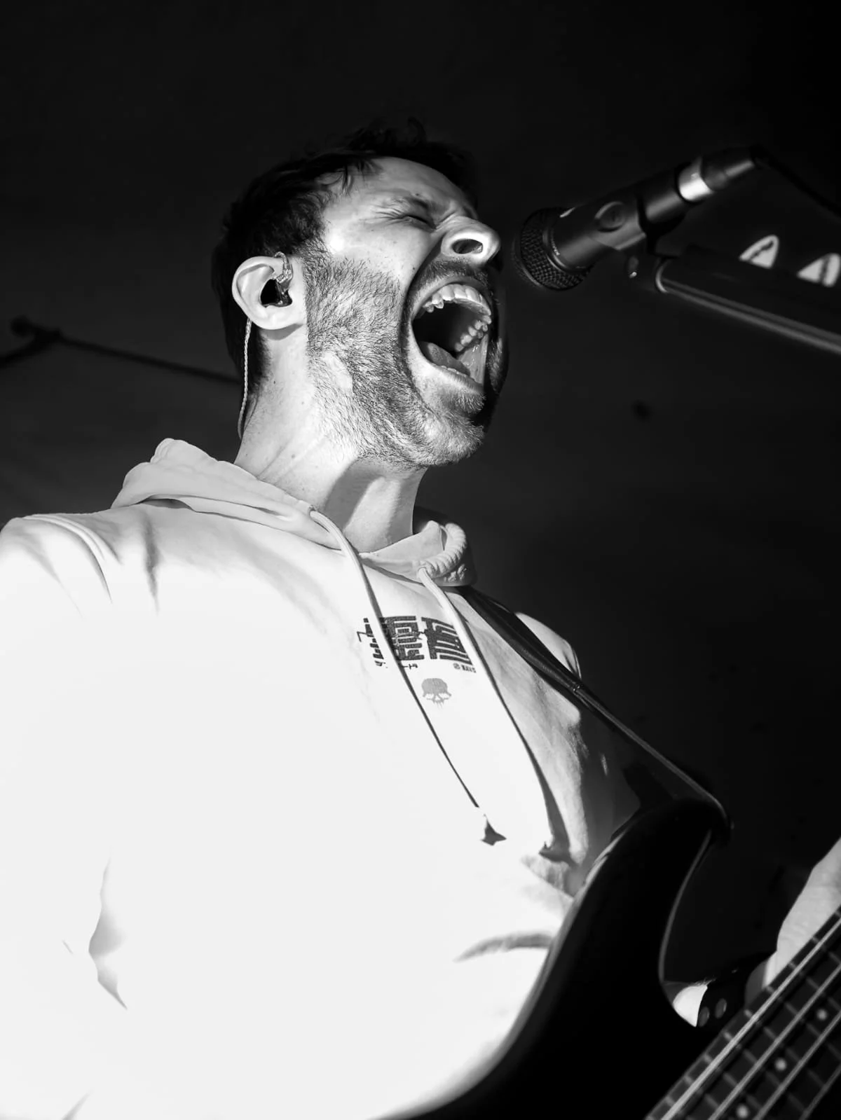 Schwarz-Weiß-Foto von Urs, der laut singt oder schreit, während er ein Mikrofon und eine Gitarre spielt, mit einem Earpiece im Ohr.