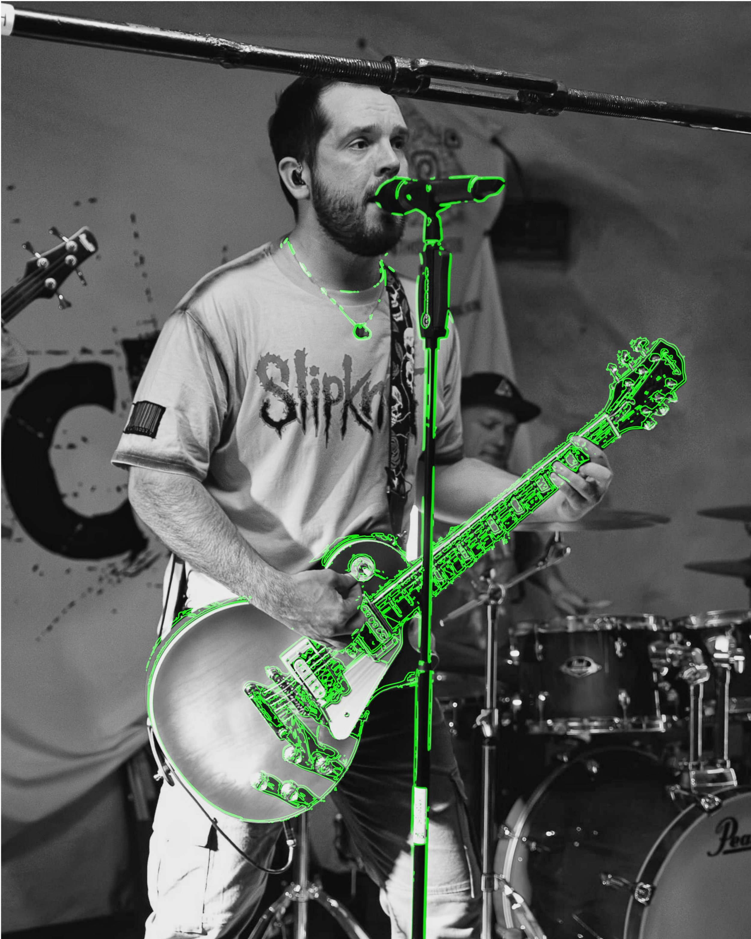 Black and white photo of a man playing the guitar, singing into a microphone, with a drum set in the background. The guitar and microphone are outlined in bright green digital annotation.