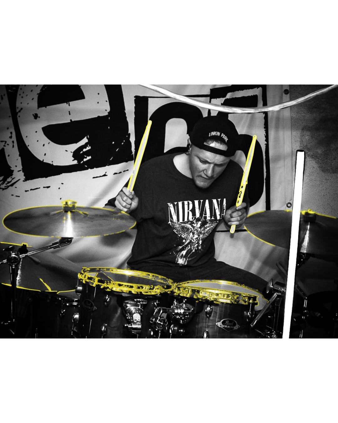 A man playing drums at a music venue, wearing a black Nirvana T-shirt and a black cap turned backwards.