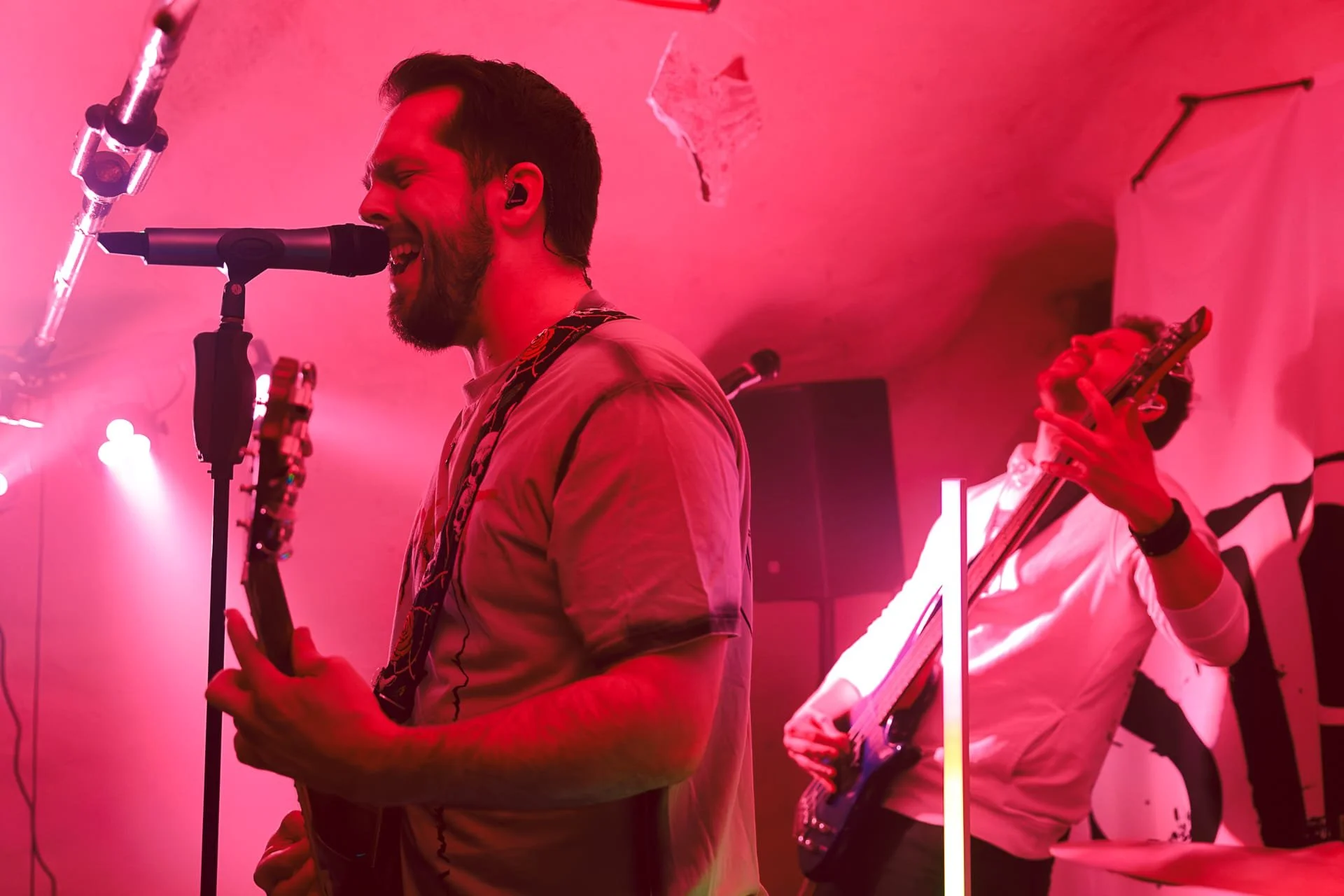 Niklas und Urs spielen Gitarre und singen in einem pink beleuchteten Raum, einer trägt ein In-Ear-Monitor.