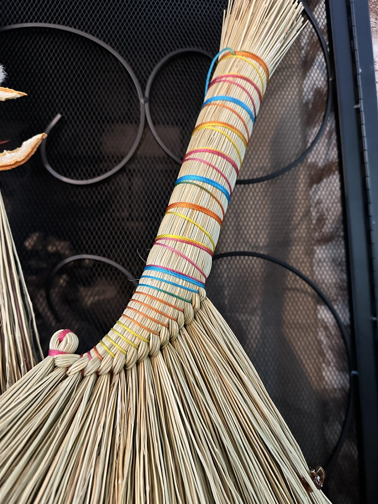 Close-up of a woven straw sculpture or art piece with colorful rubber bands, on a black mesh surface.