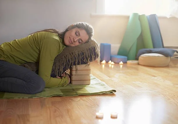 A woman practicing yoga or meditation using a stacked cushion for support on a yoga mat.