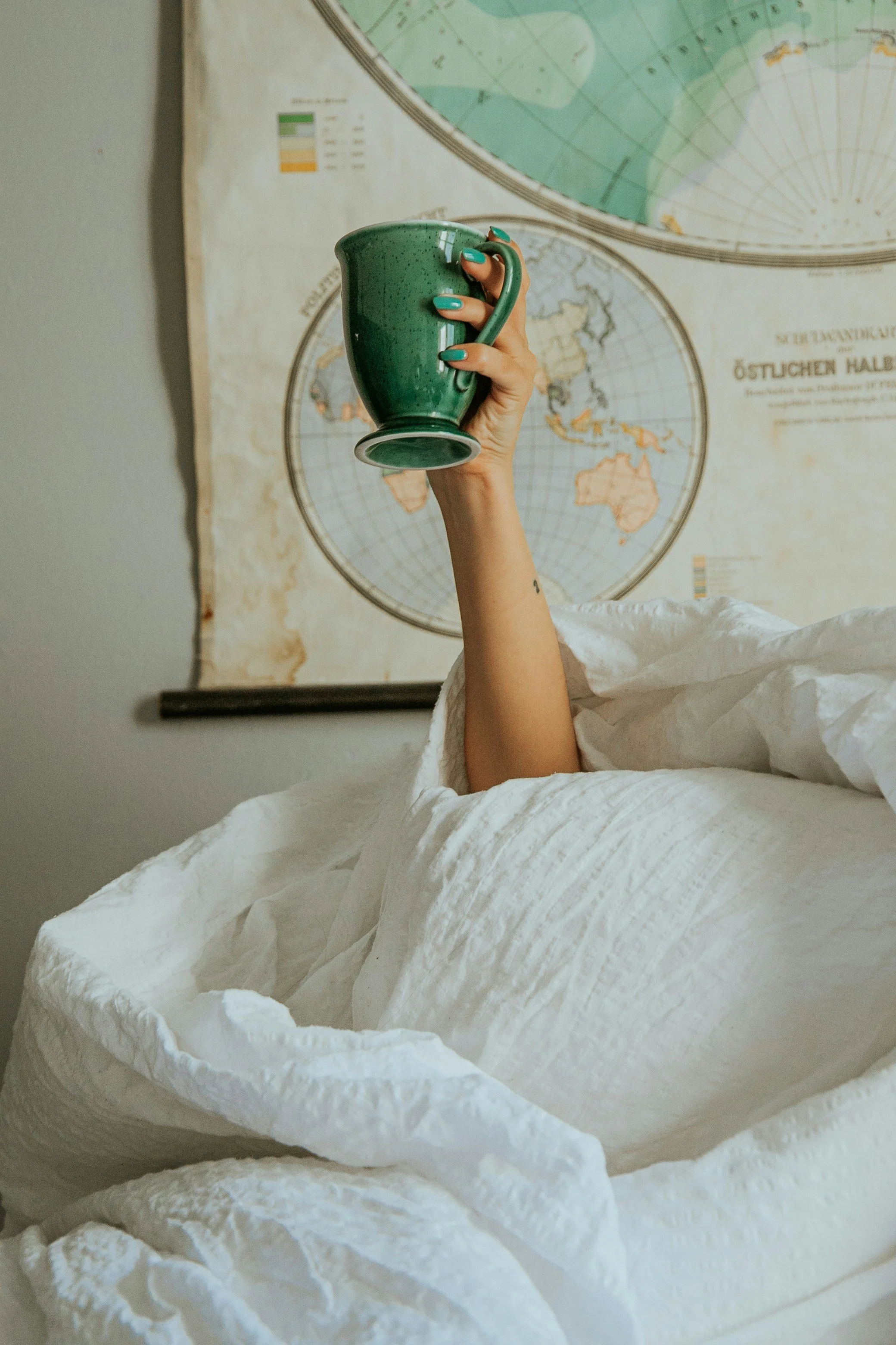 A person holding a green ceramic mug with nail polish matching the mug, in front of a world map poster on the wall.