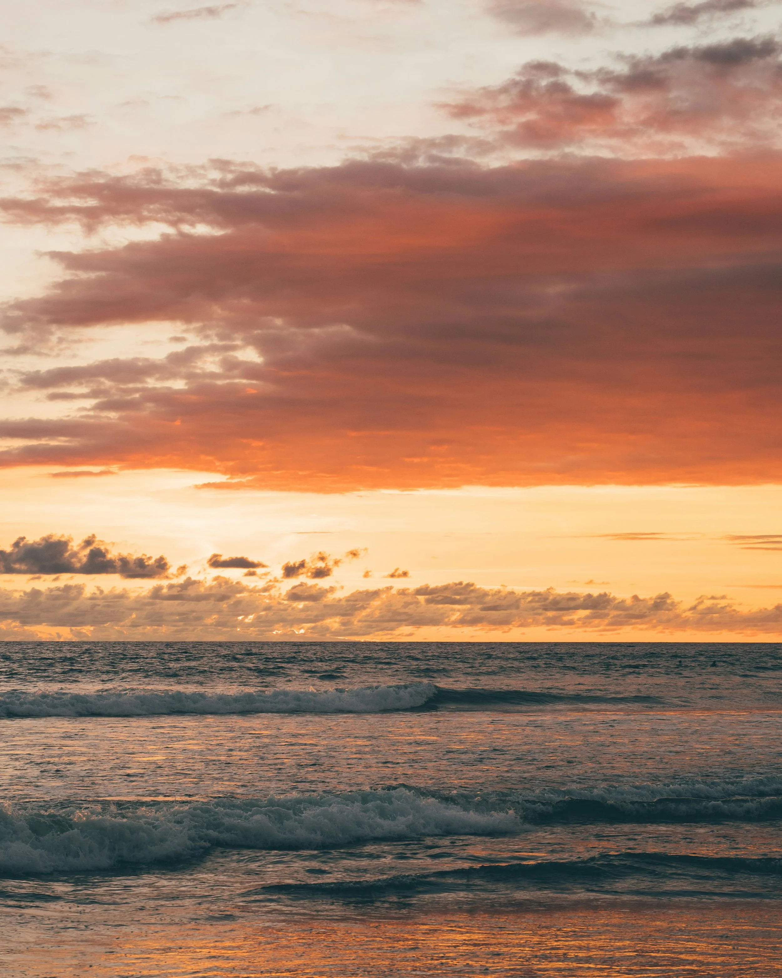 A sunset over the ocean with waves and a colorful sky filled with clouds.
