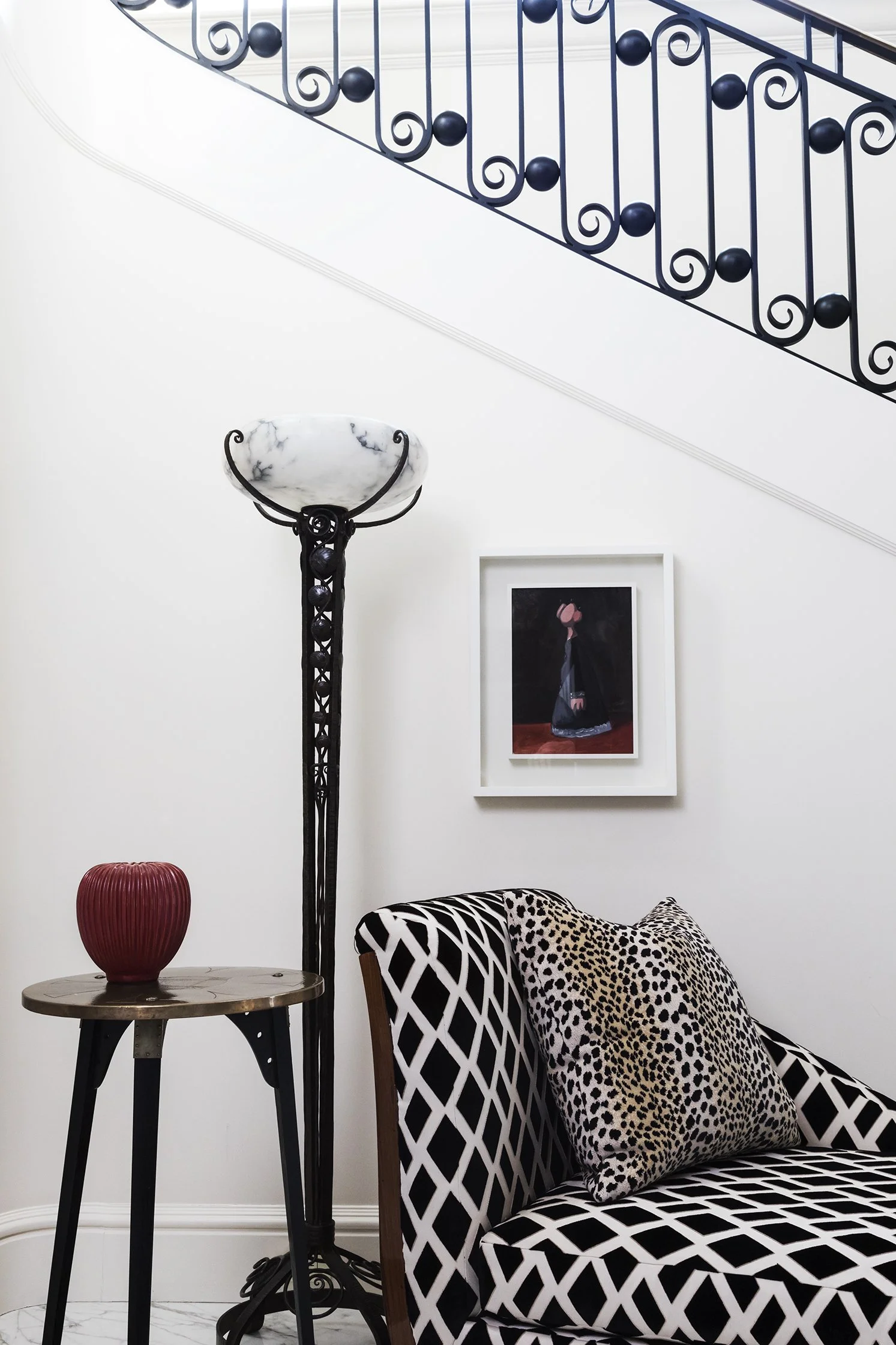 Staircase hall with ornate black wrought iron railing, Art Deco marble floor lamp, geometric black and white chaise lounge, and small framed artwork, New York Townhouse