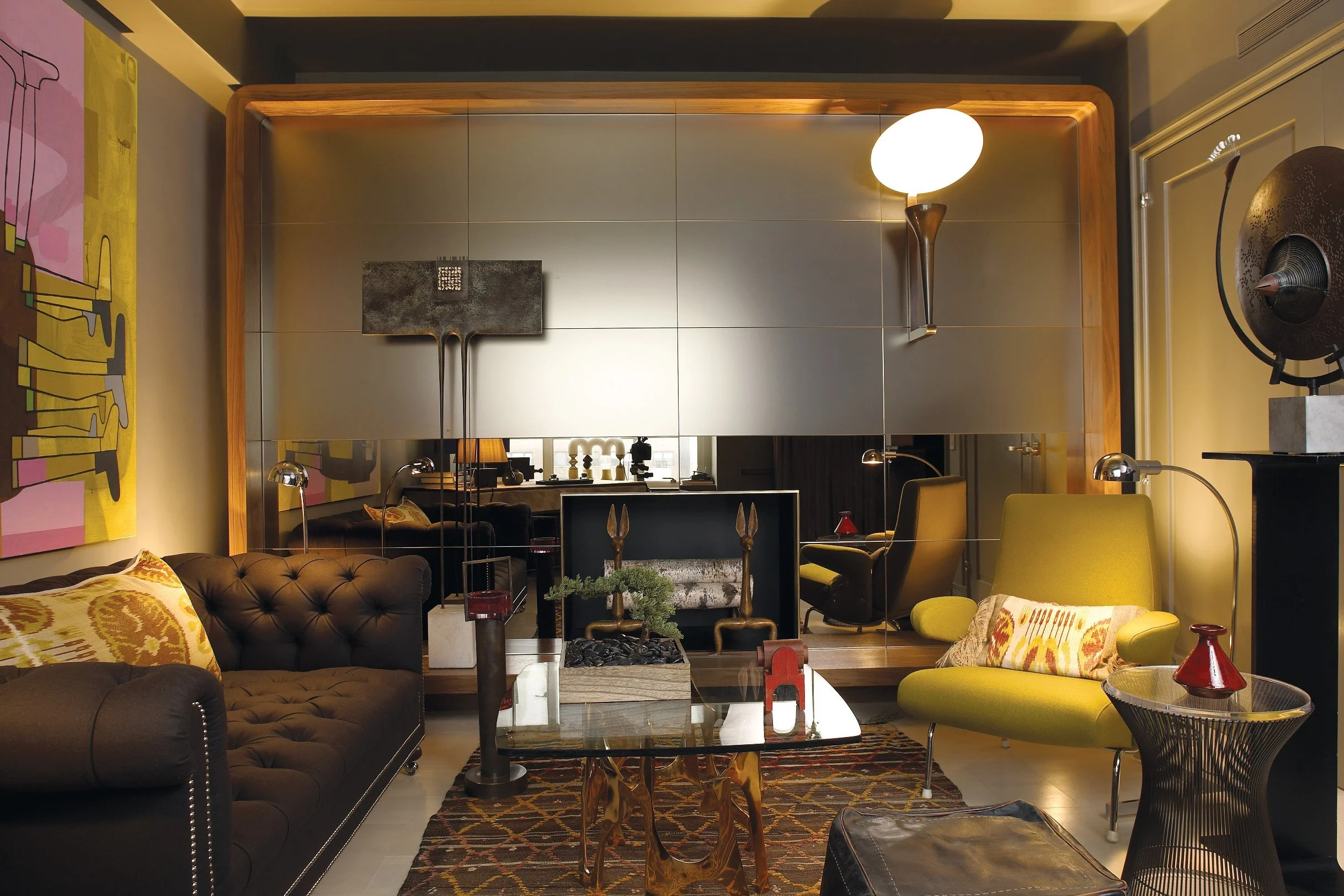 Eclectic living room with tufted chocolate brown sofa, mirrored wall panels, yellow armchairs, glass coffee table, and bold contemporary artwork in warm amber tones