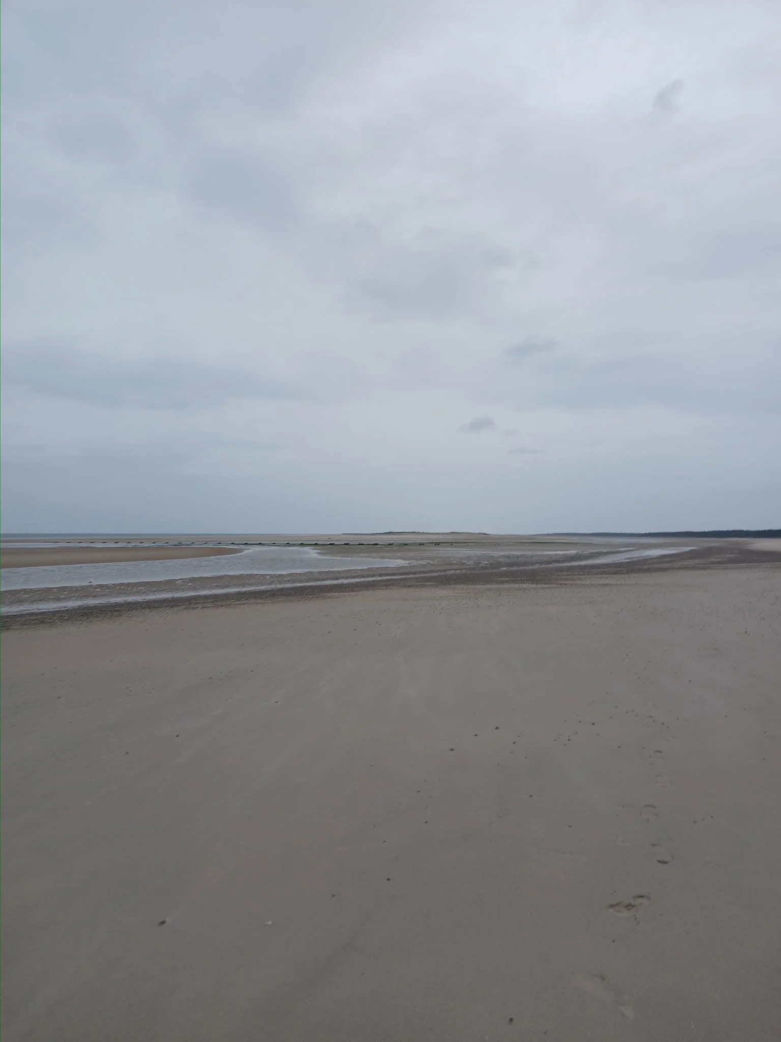 Overcast sky with cloudy weather over a sandy beach with footprints and tide lines.
