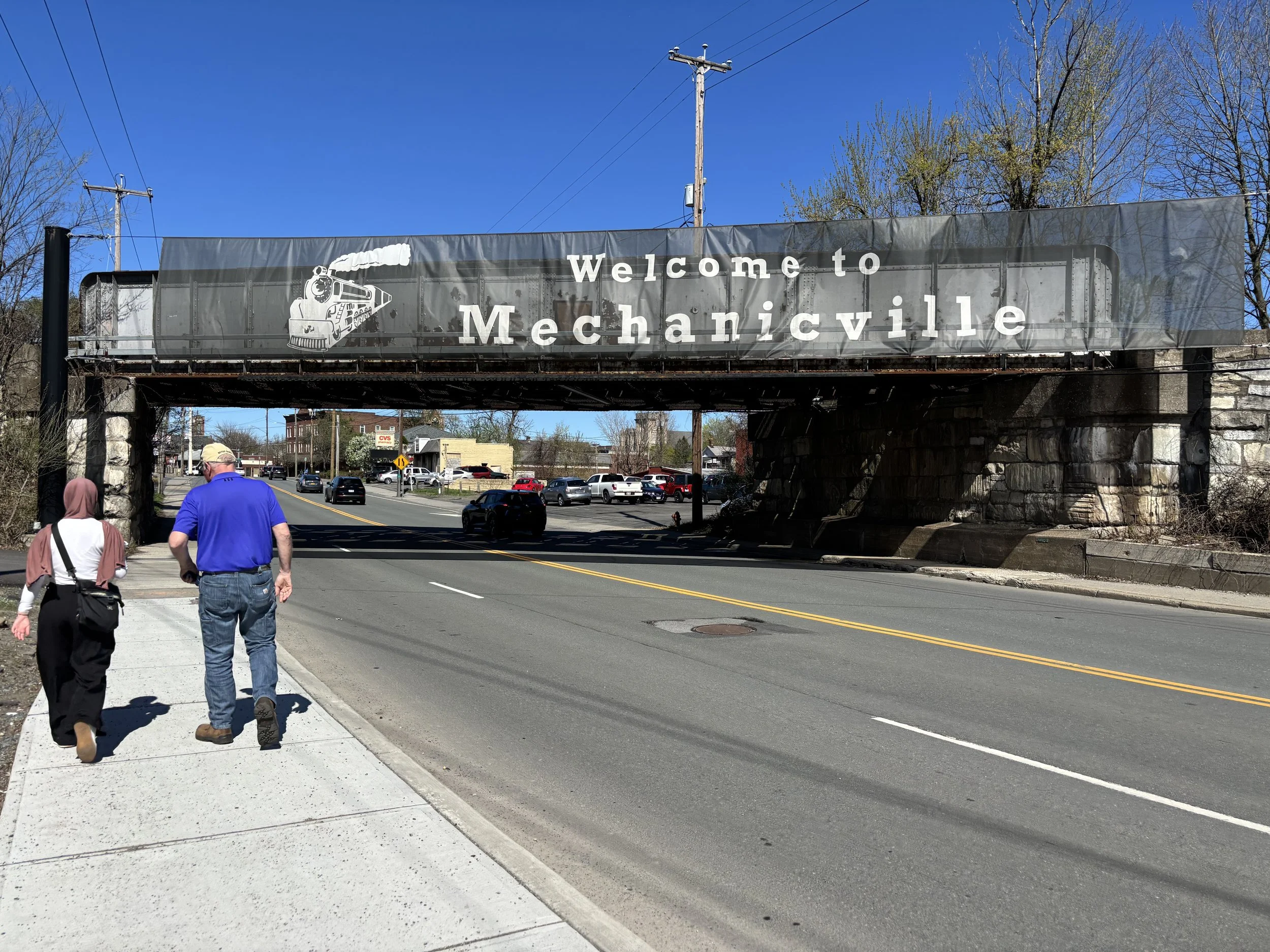 Two people walking toward the Mechanicville bridge spanning the main drag.