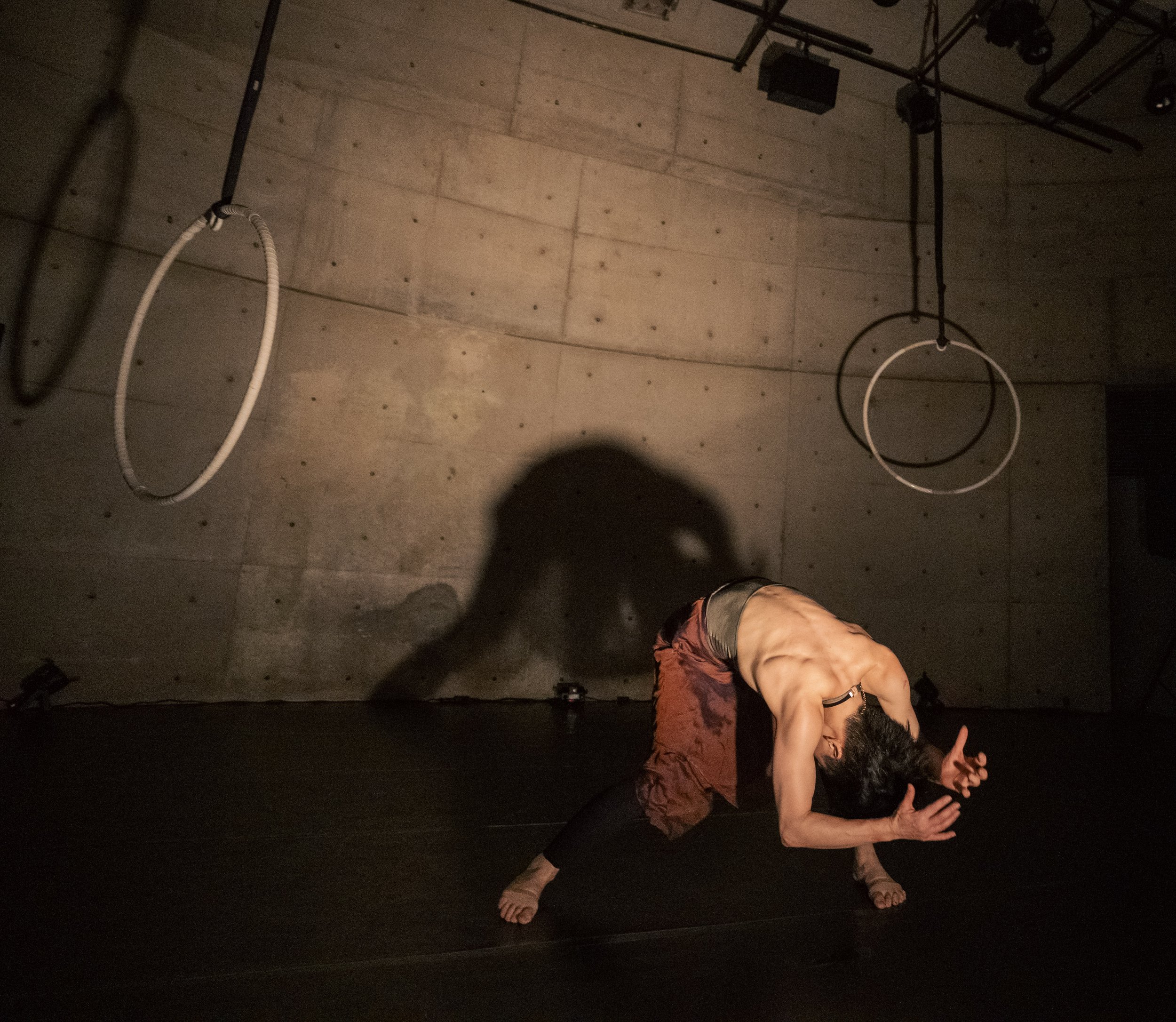 A man practicing yoga or stretching on the floor, seen from above, with a concrete wall and gym equipment in the background.